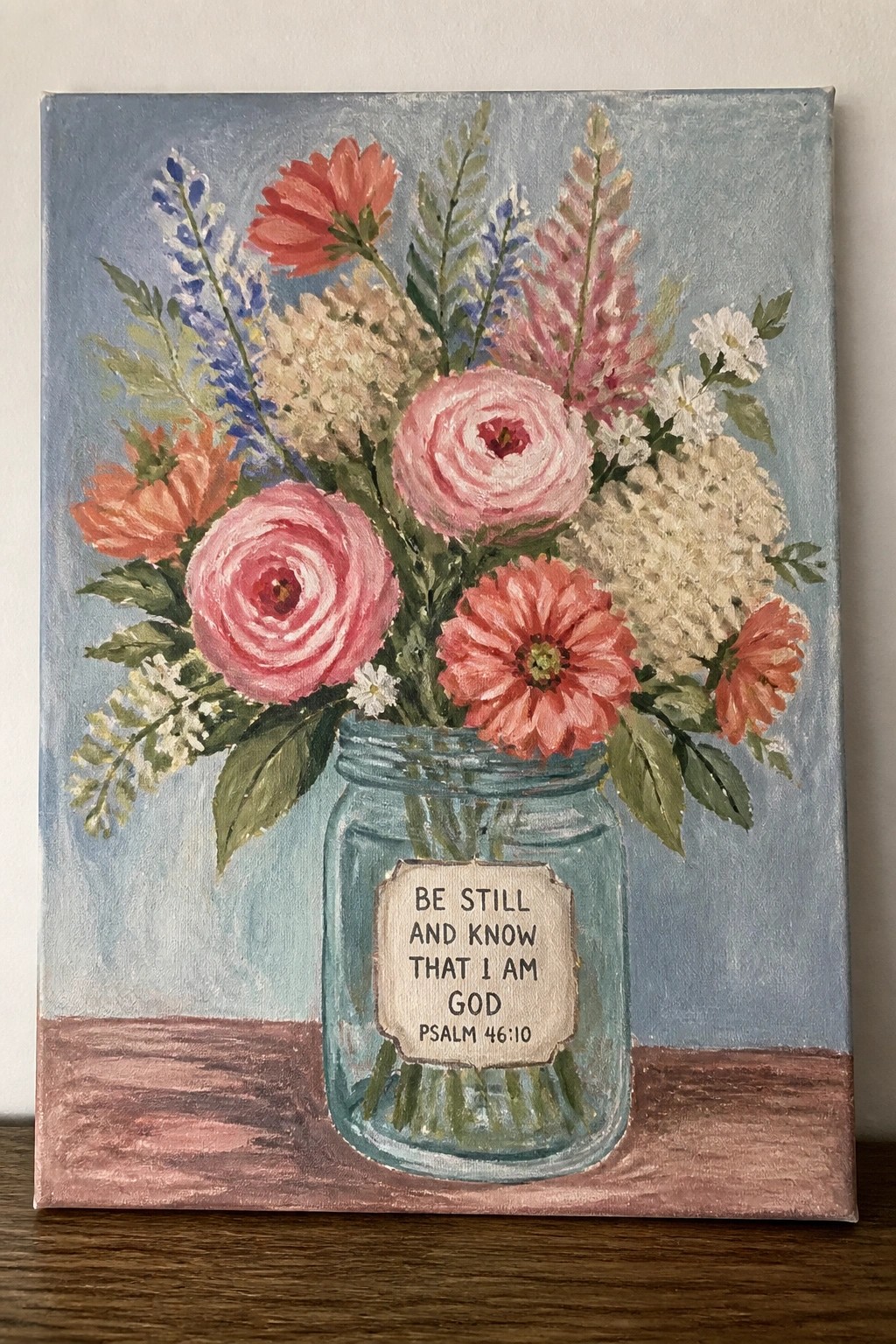 Vibrant floral bouquet in blue mason jar with Psalm 46:10 label on wood.