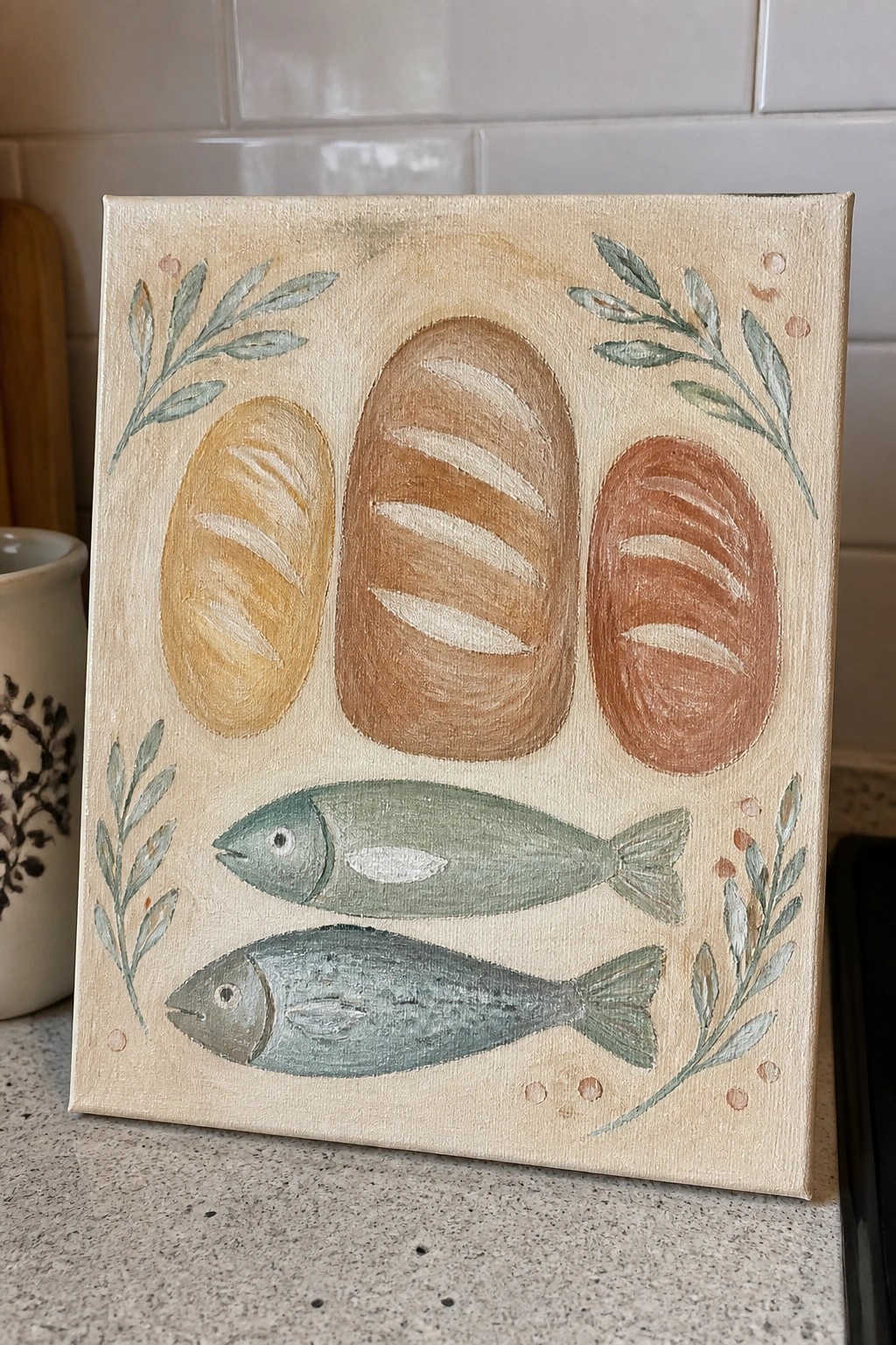 Canvas painting of three bread loaves above two fish with leafy branches