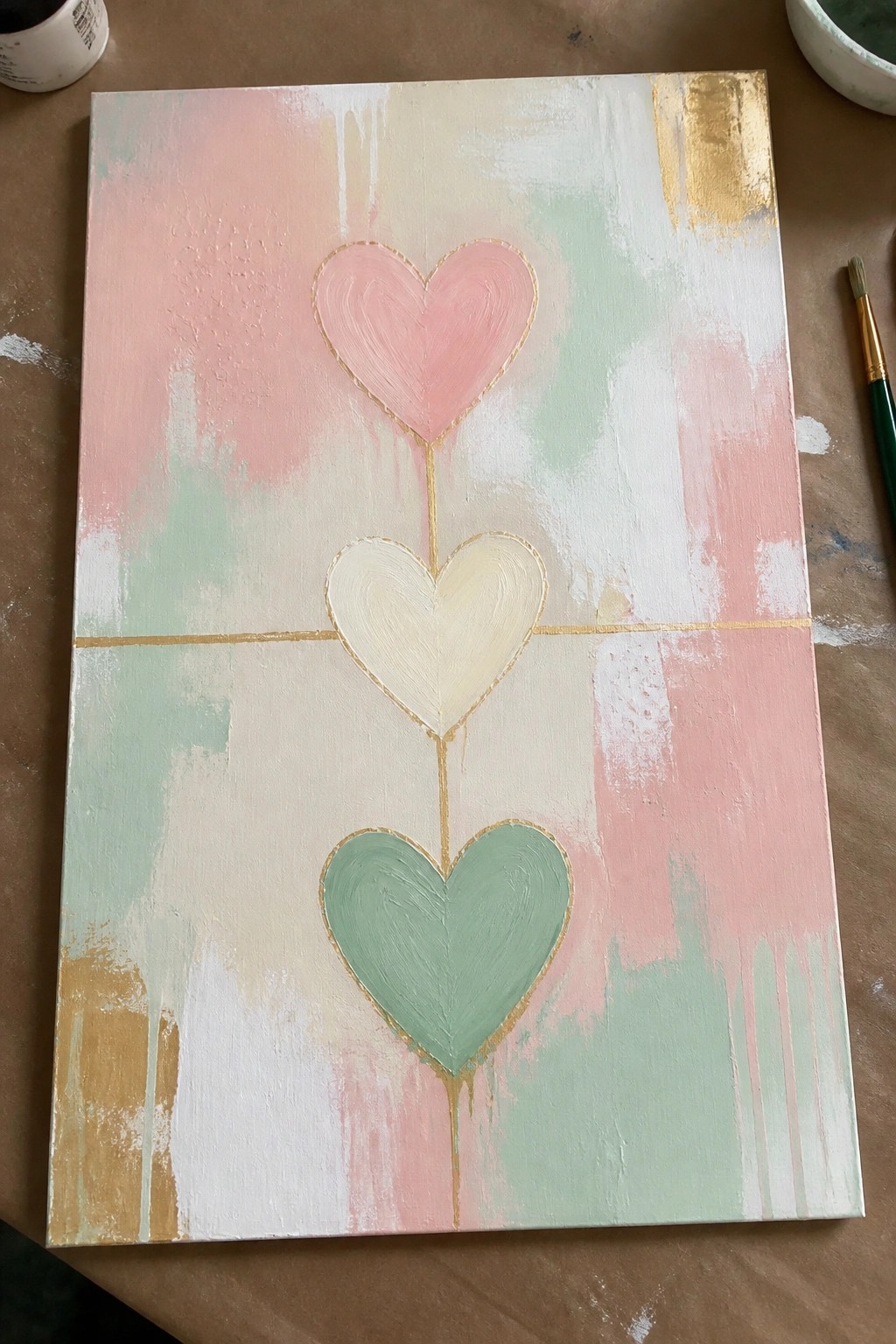 Abstract painting of three stacked pastel hearts in pink, cream, and green with gold lines.