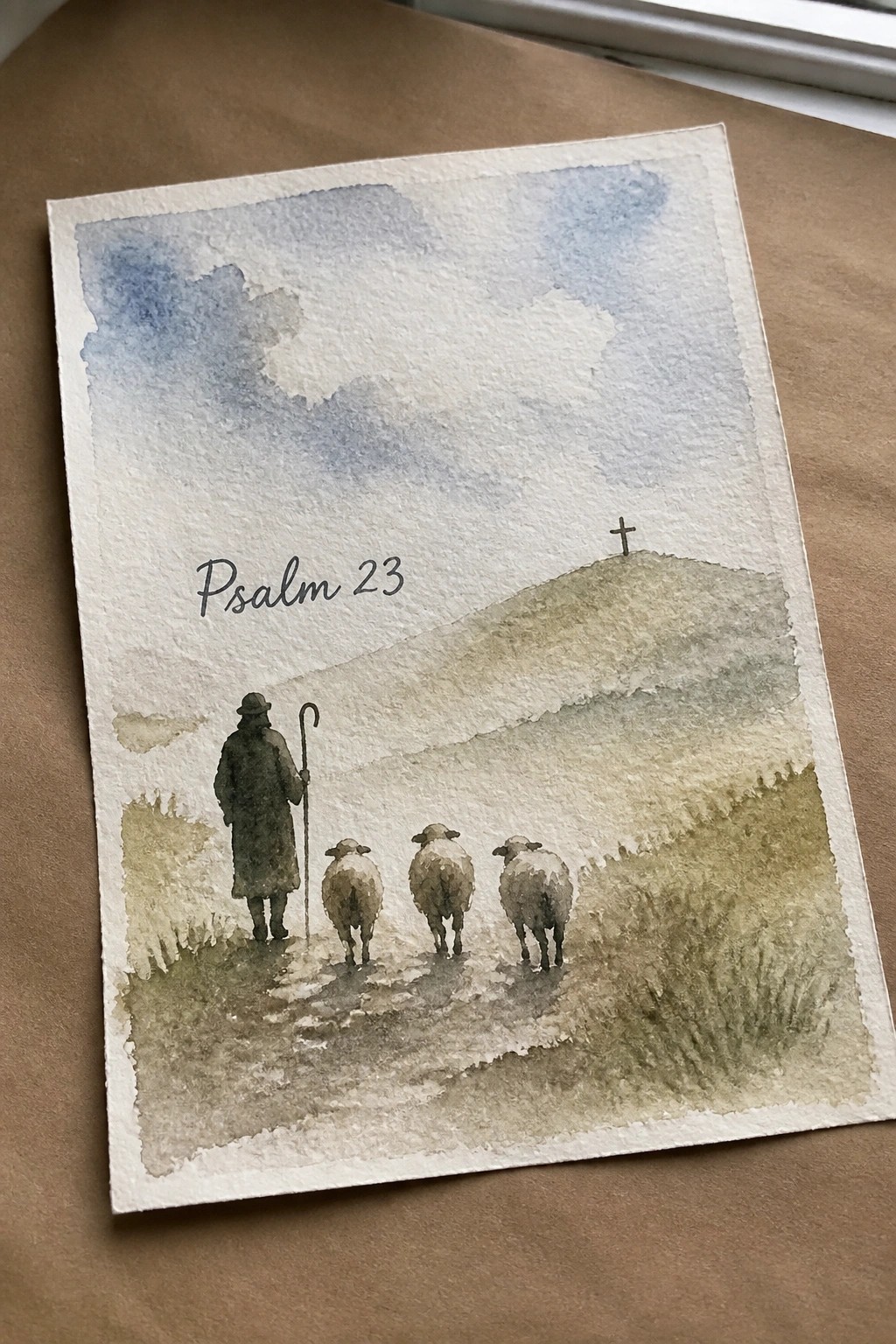 Watercolor of shepherd leading three sheep on path to cross-topped hill with Psalm 23 text.