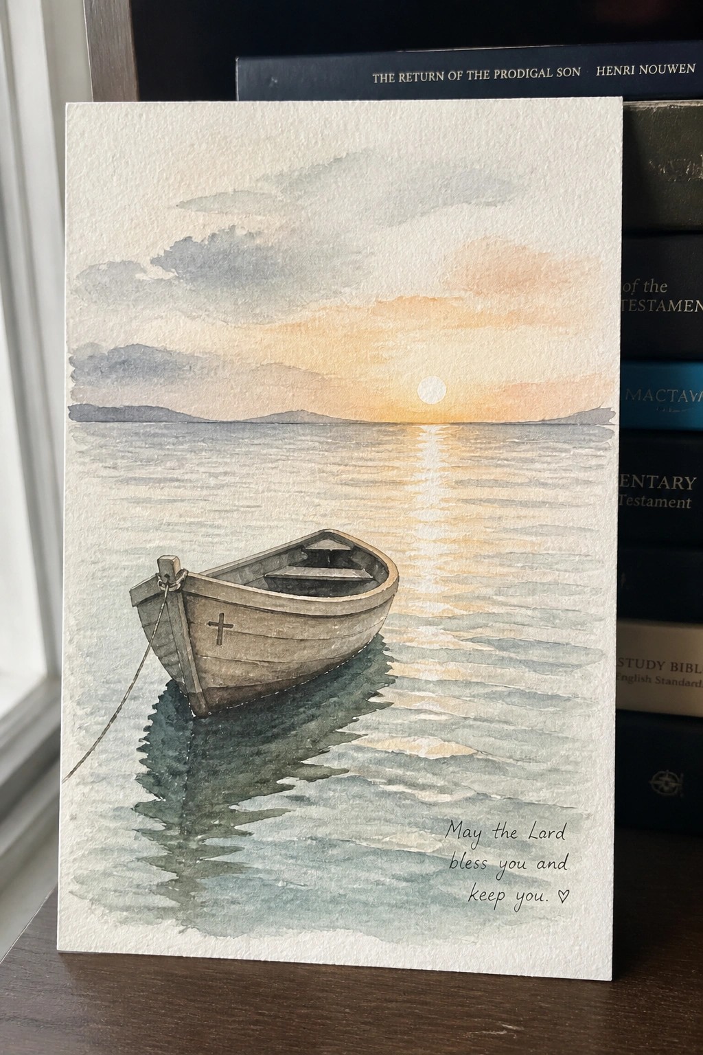 Watercolor painting of boat with cross on calm water at sunset, with blessing text.