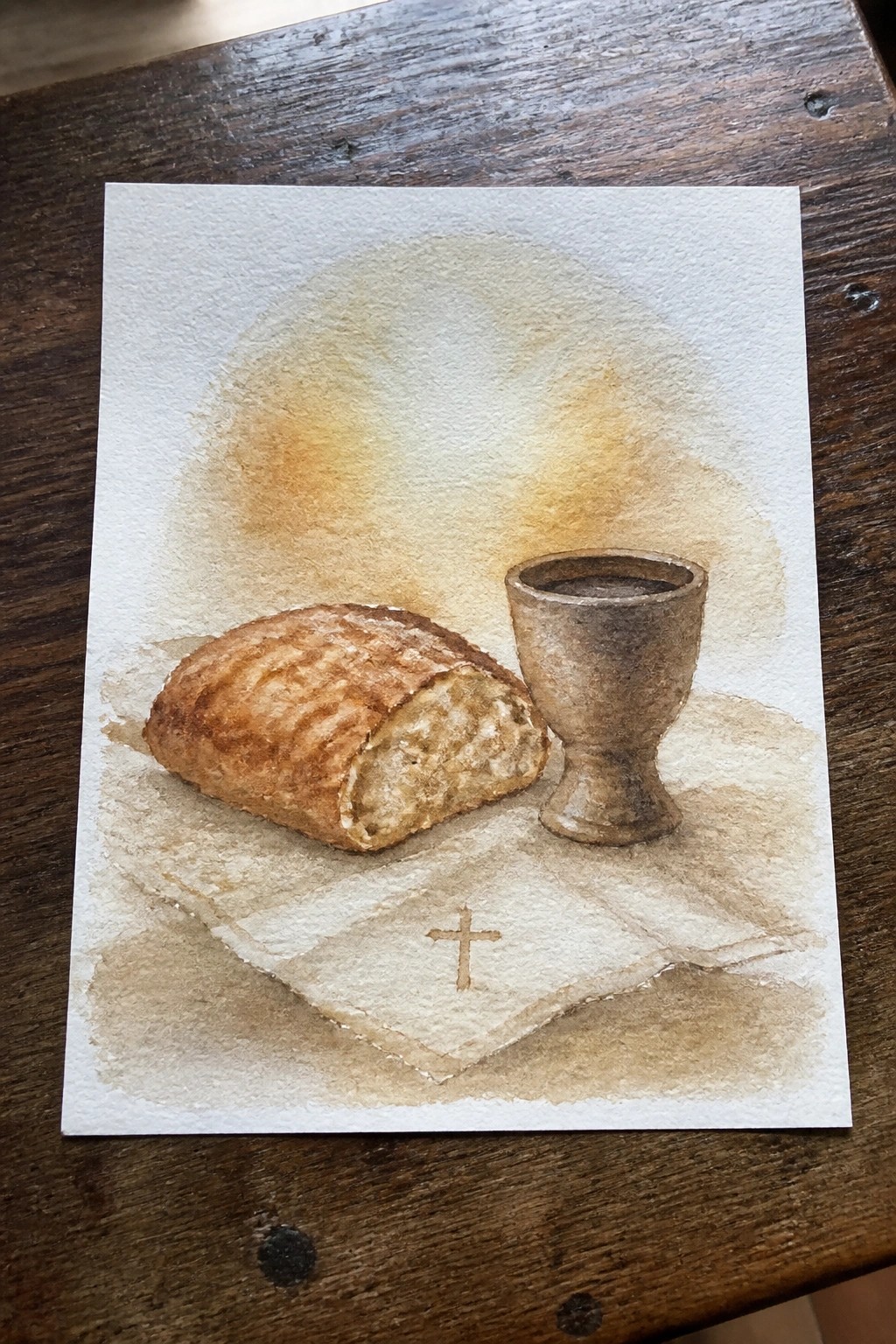 Watercolor still life of sliced bread, wine chalice, and cross on cloth.