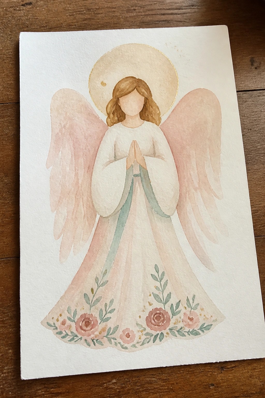 Watercolor angel with golden halo, pink wings, praying hands, and rose-trimmed gown