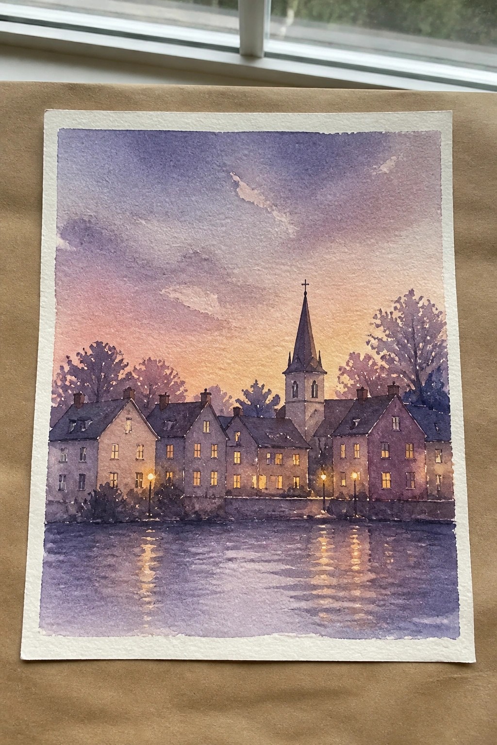 Watercolor of riverside houses with glowing windows and church steeple reflecting in water at sunset