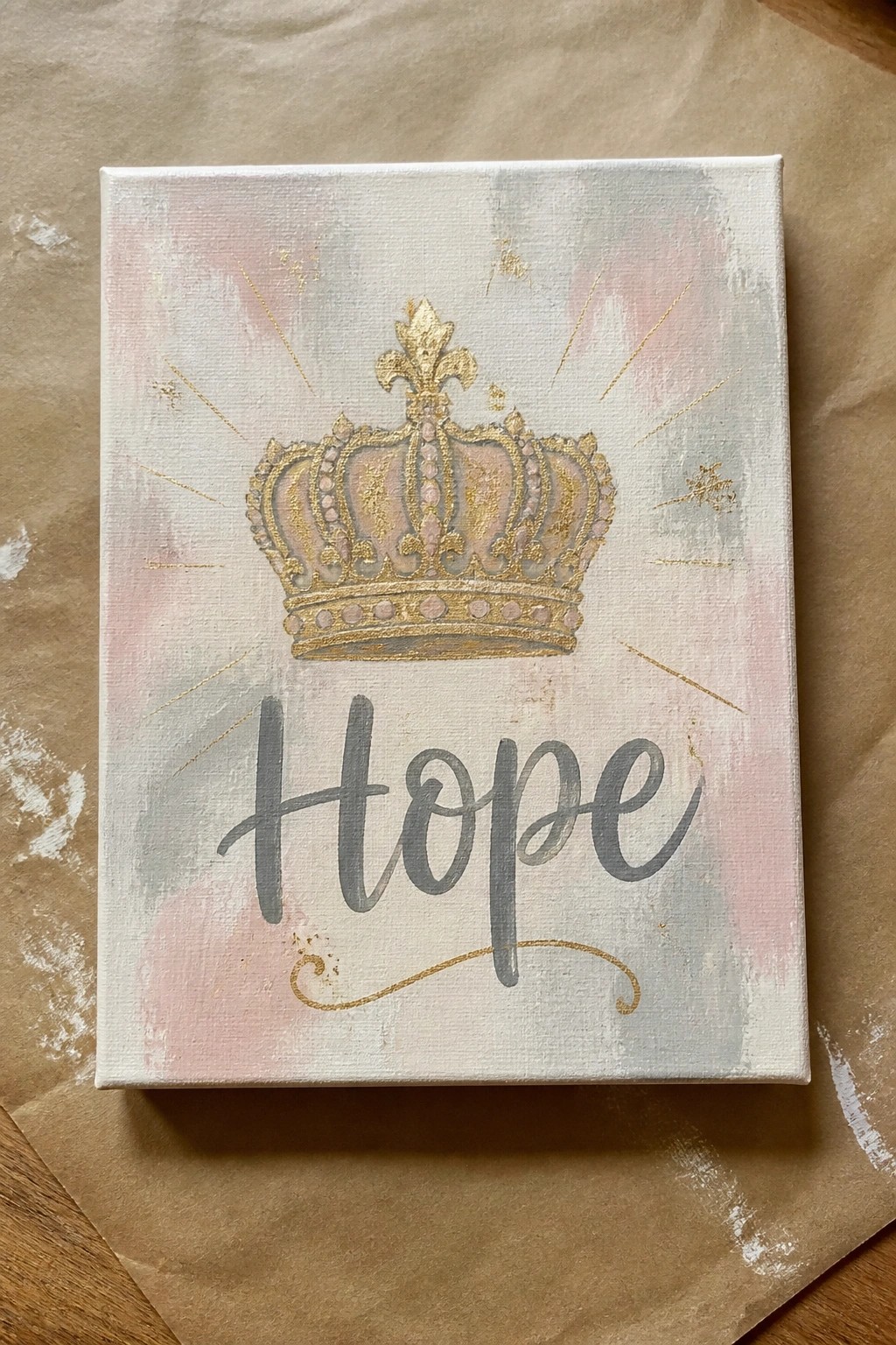 Golden crown above cursive Hope on pink-gray canvas with gold rays and sparkles