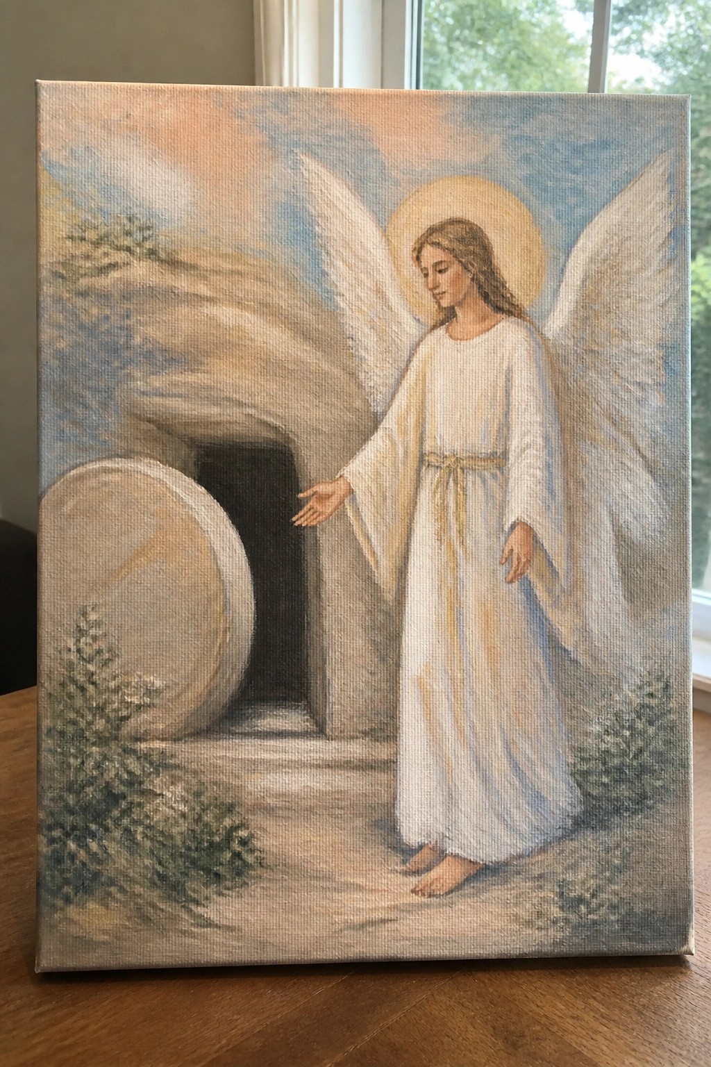 A painting of an angel with wings and a halo standing outside an empty stone tomb with the round door rolled aside.