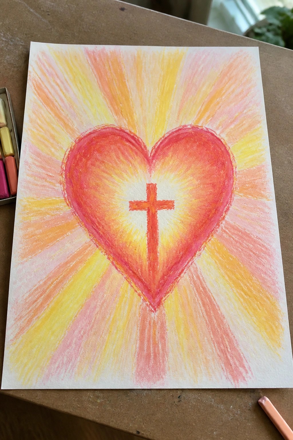 Vibrant crayon drawing of red heart with orange cross and radiating yellow-pink rays.