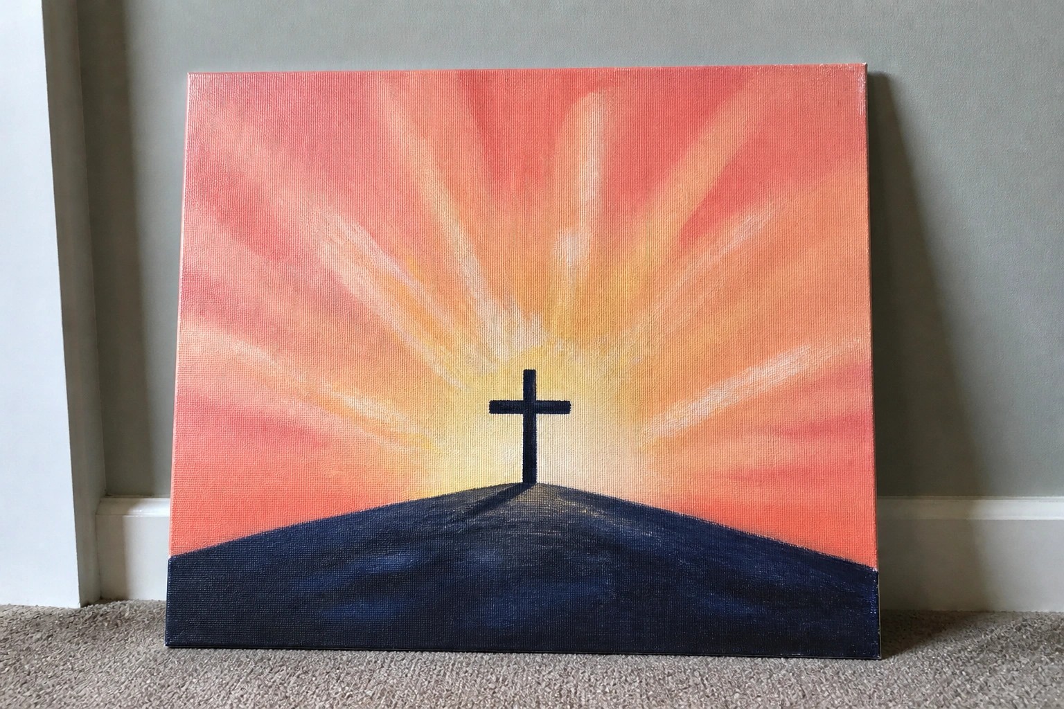 Black cross atop dark hill against vibrant orange-pink sunset with radiating light rays.