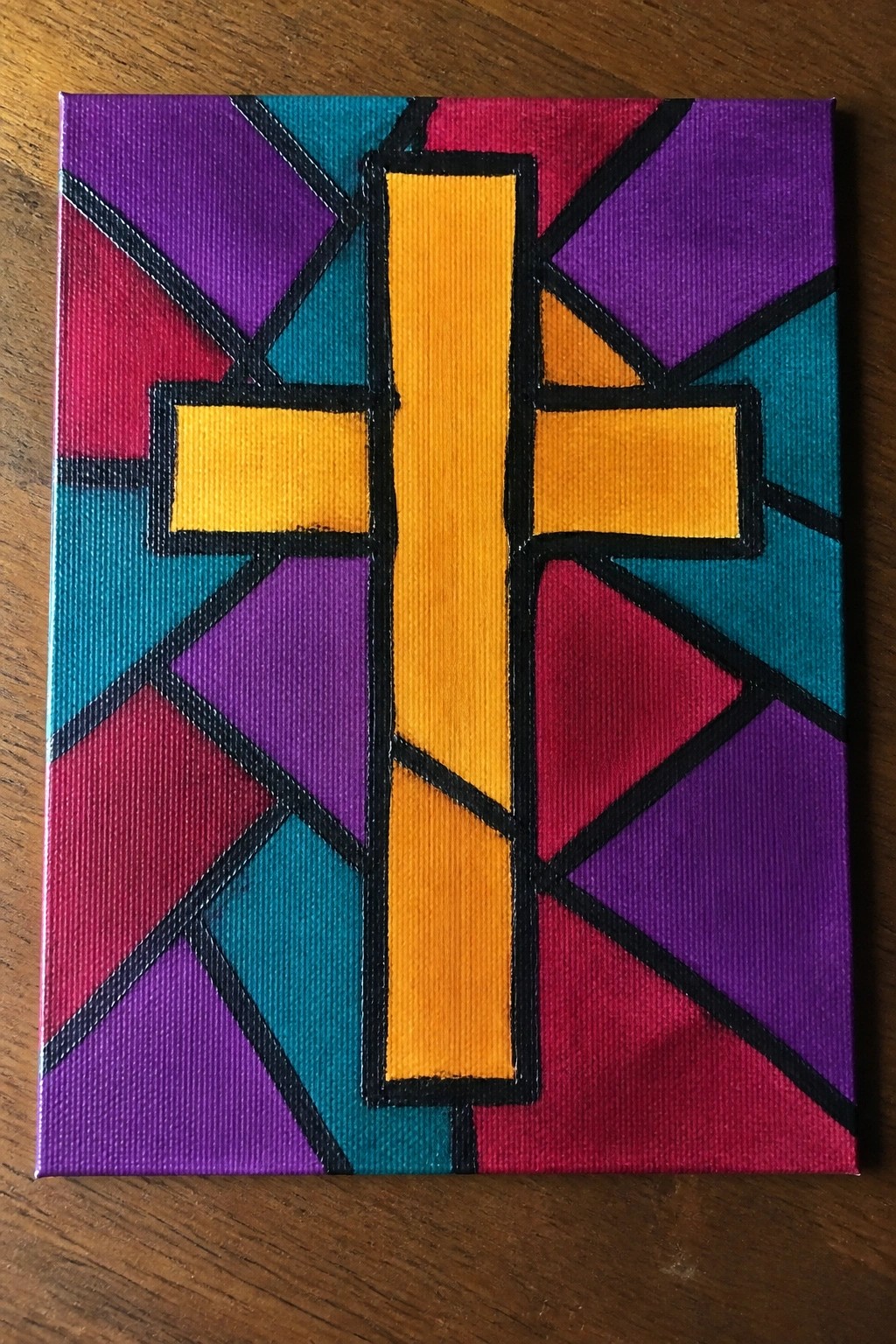 Vibrant yellow cross with black outline on multicolored geometric canvas painting.