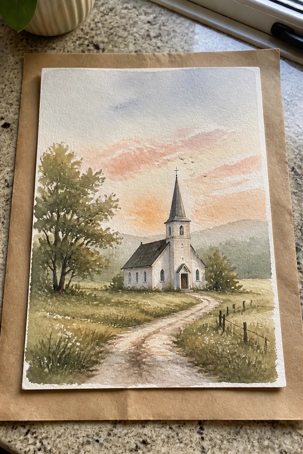 Watercolor painting of a white church with a steeple along a dirt path in a green field under a pink and orange sunset sky.