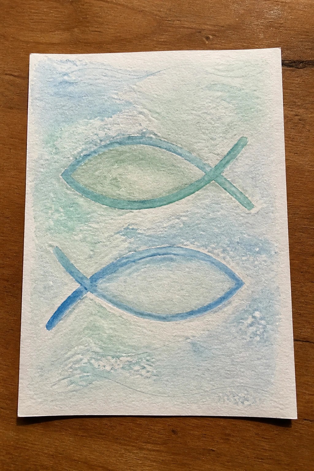 Two watercolor ichthys fish symbols in teal and blue on a light blue-green background with faint wave lines.