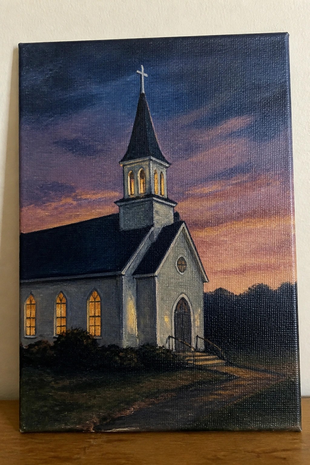 Oil painting of white church with glowing windows and steeple at vibrant sunset.