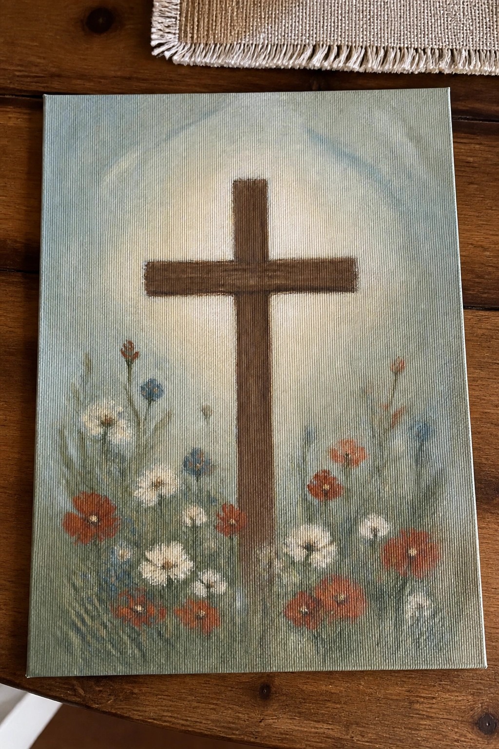 Wooden cross with red poppies and white daisies on light blue canvas.