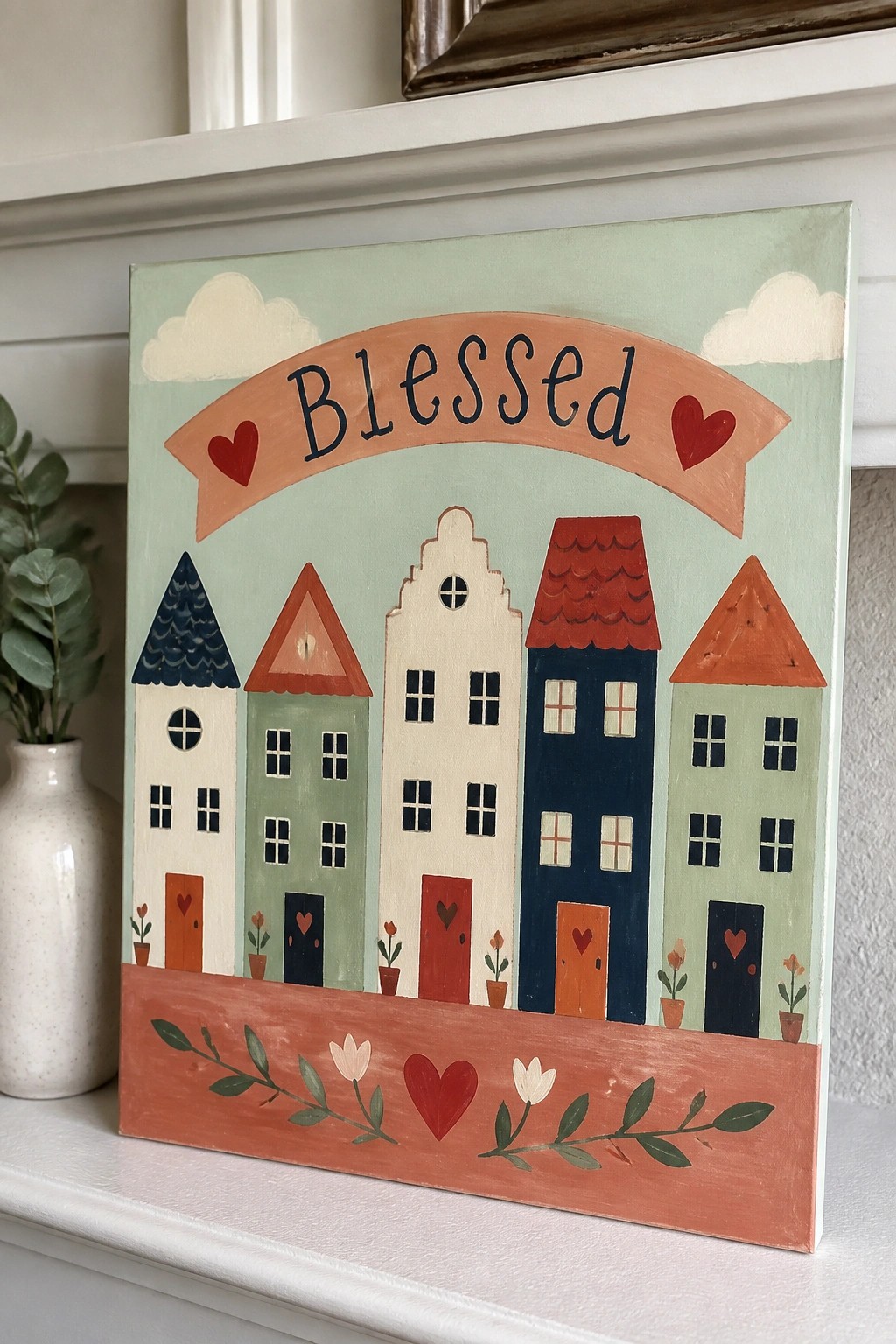 Pastel houses under Blessed banner with red hearts and flowers on white mantel.