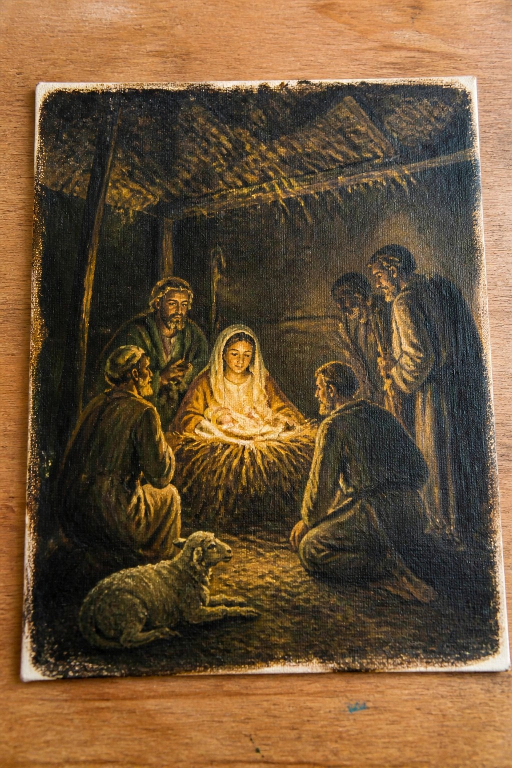 Warm-toned painting of robed figures around infant in straw manger with resting sheep.