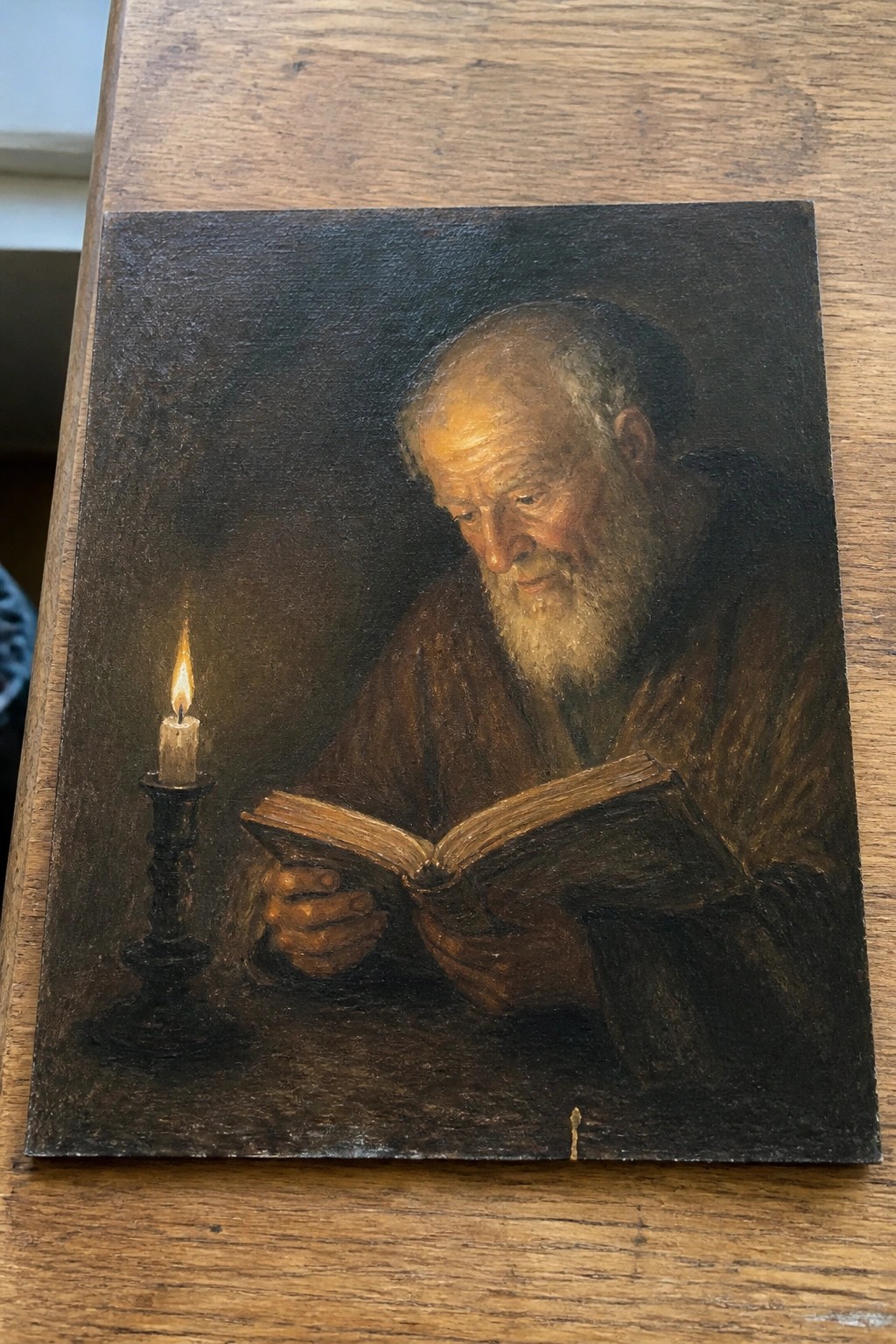 Elderly bearded man in brown robe reads open book by candlelight.