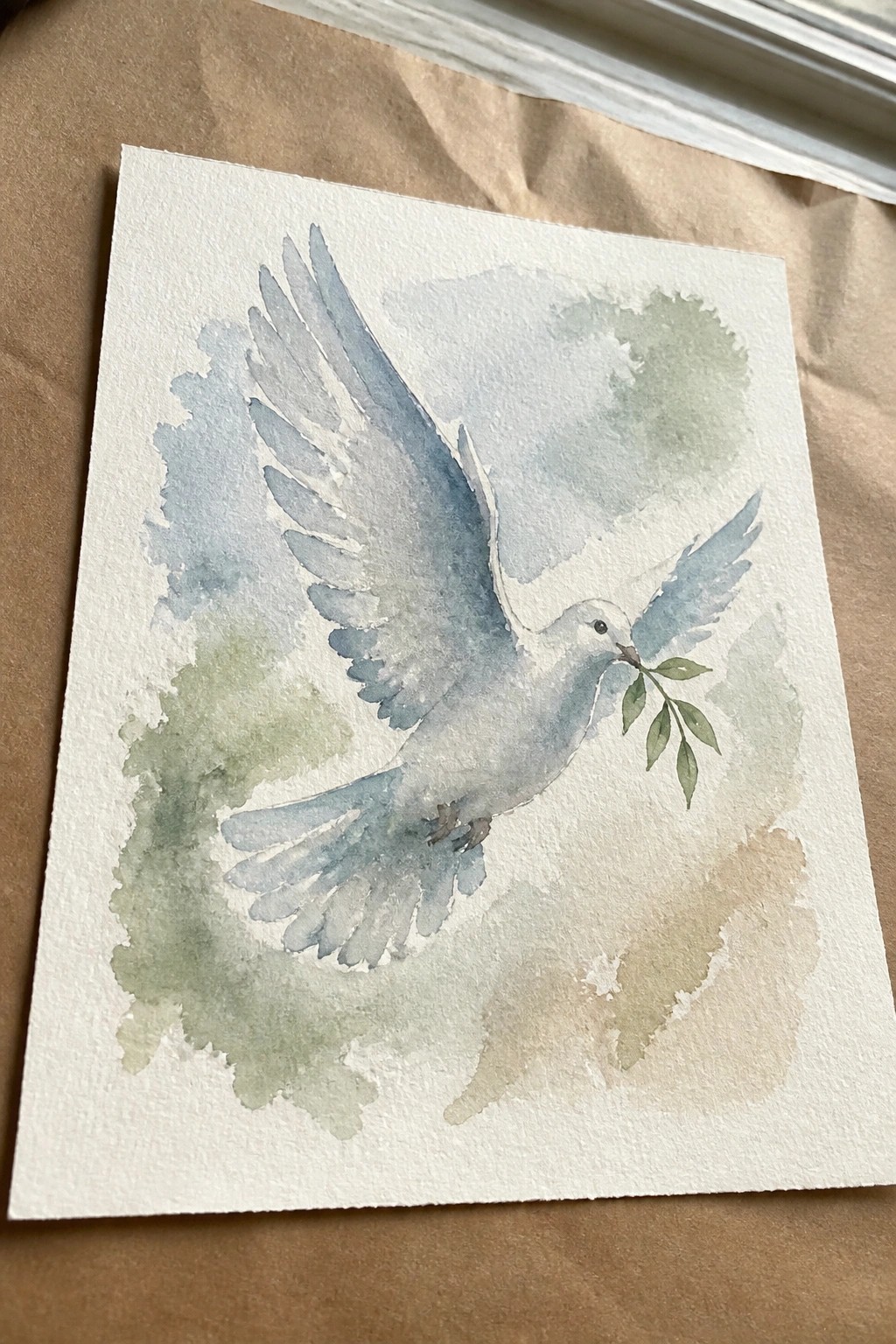 Watercolor of a white dove in flight clutching a green olive branch.