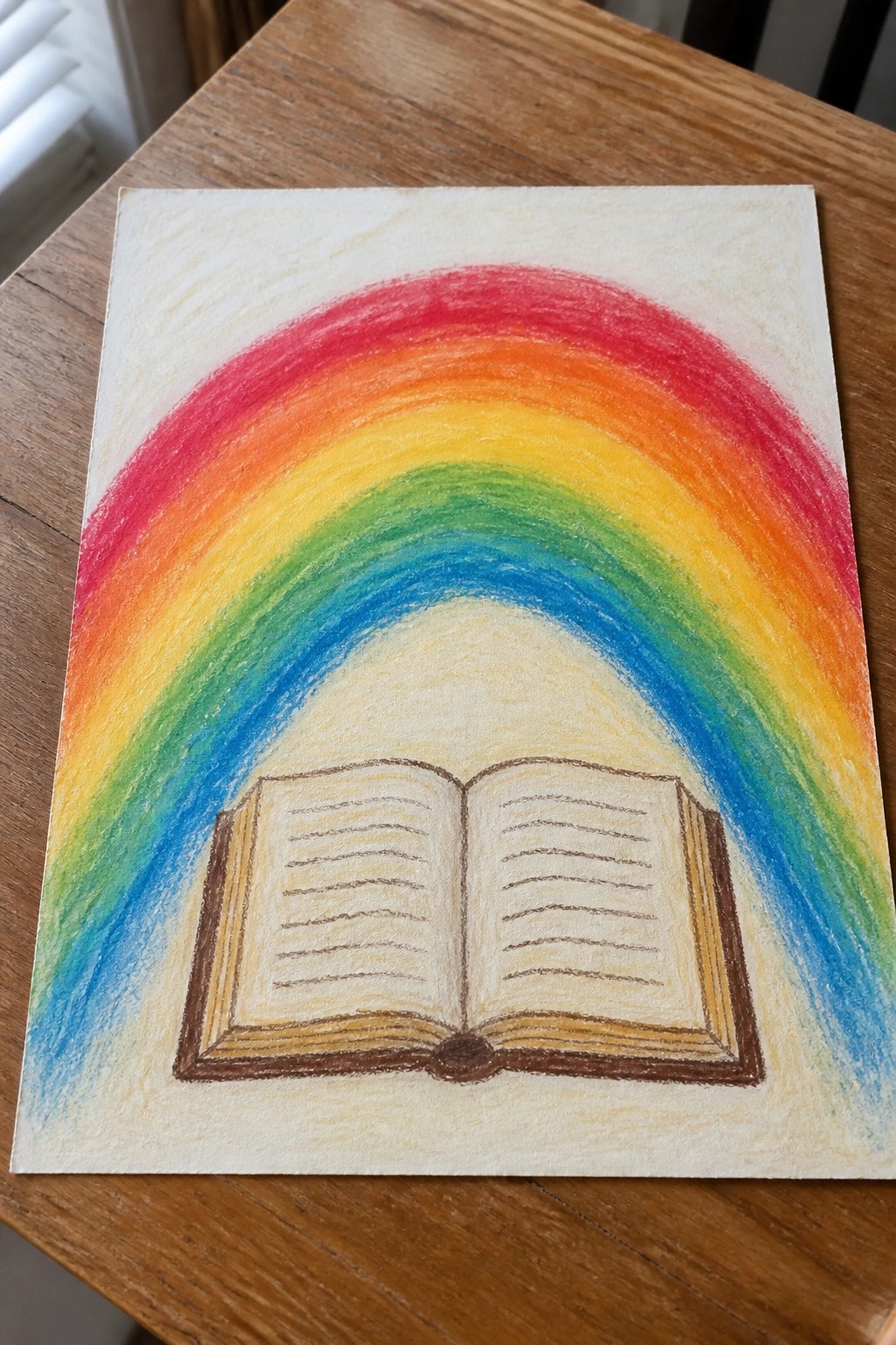 Colored pencil drawing of open book beneath vibrant rainbow on wooden table.