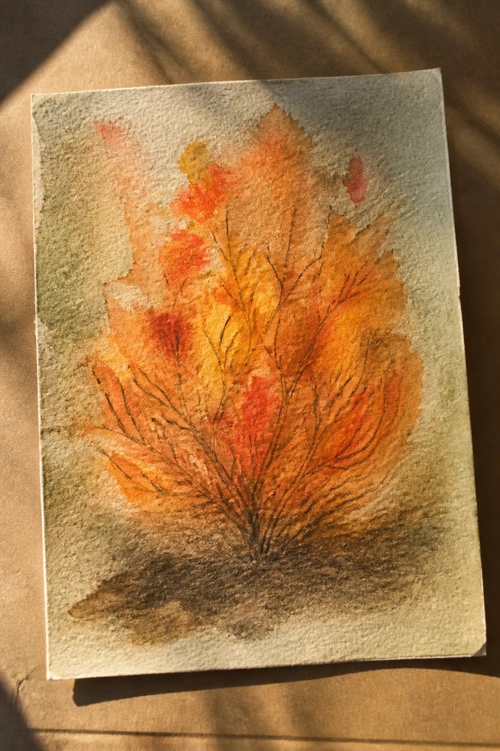 Watercolor painting of a tree with orange red and yellow autumn leaves and dark branches on textured paper.