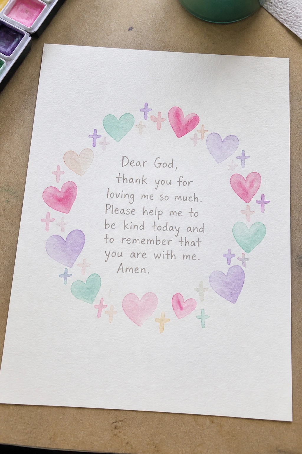 Watercolor hearts and crosses circle a handwritten prayer on white paper.