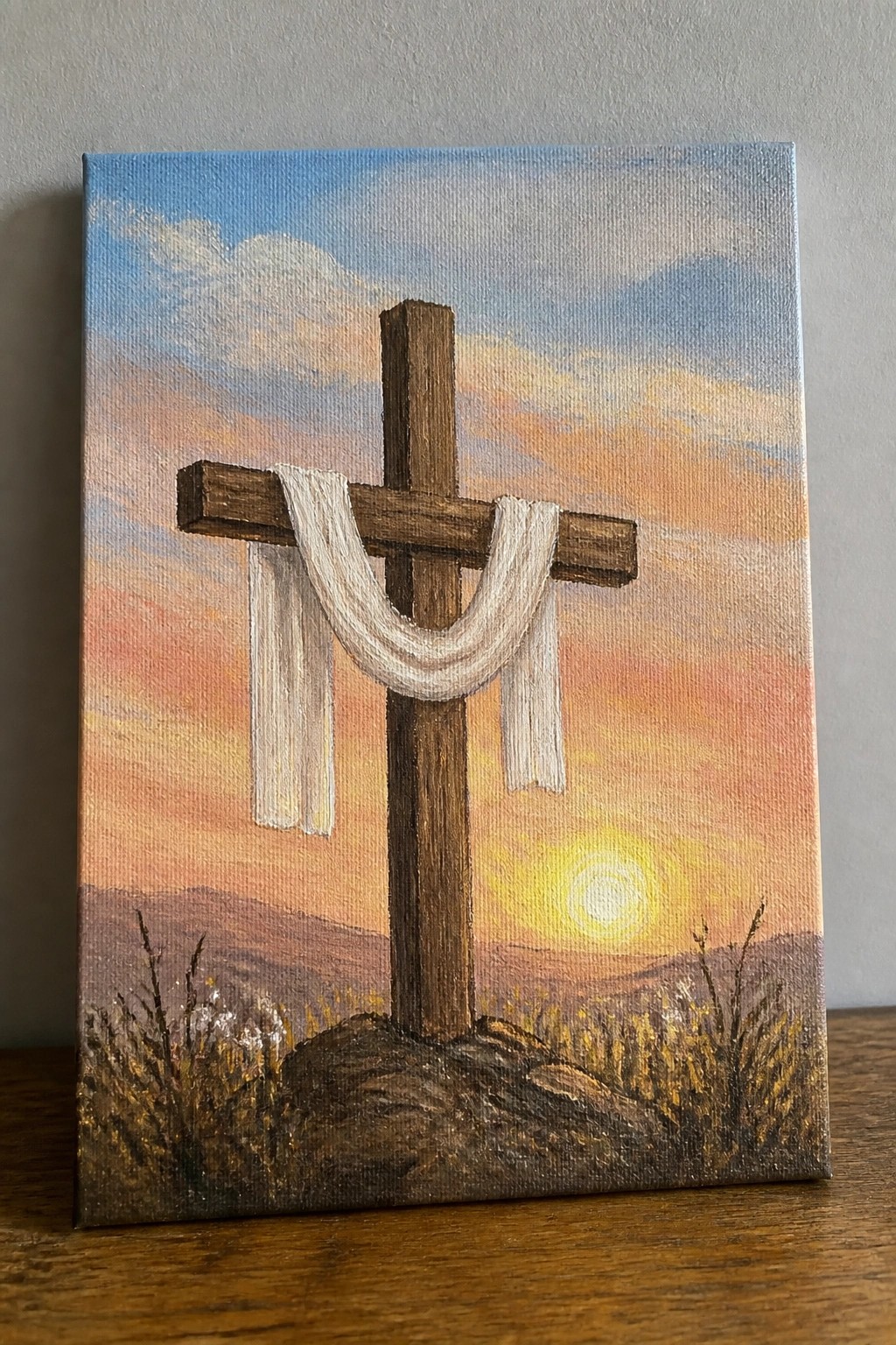 Wooden cross draped with white cloth on rocky hill at vibrant sunset