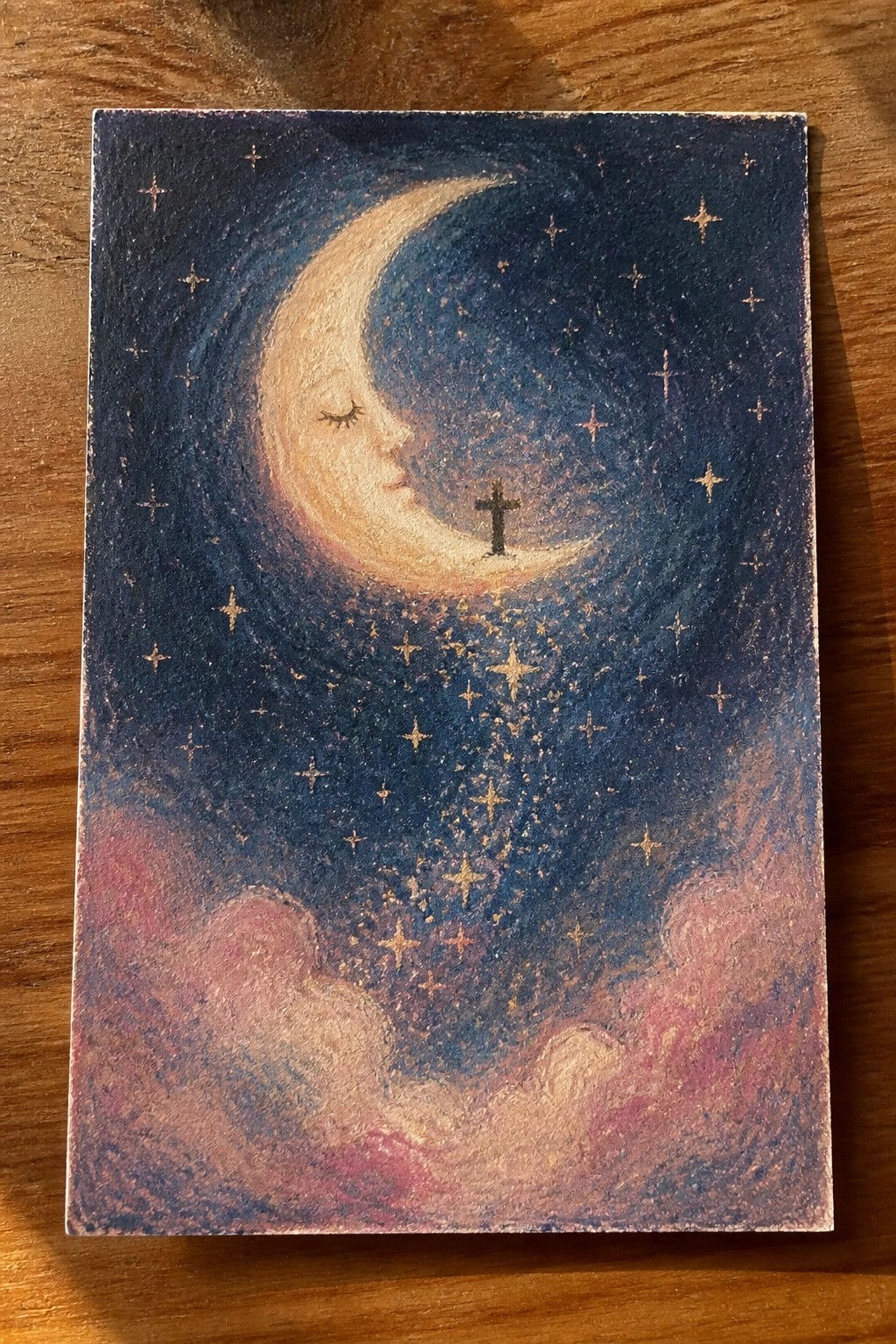 Crescent moon with face beside cross in starry blue sky above pink clouds.