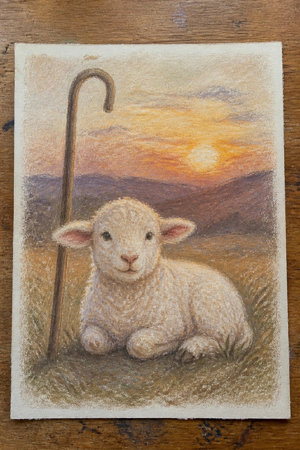 White lamb resting beside shepherd's crook on grassy hill under orange sunset sky