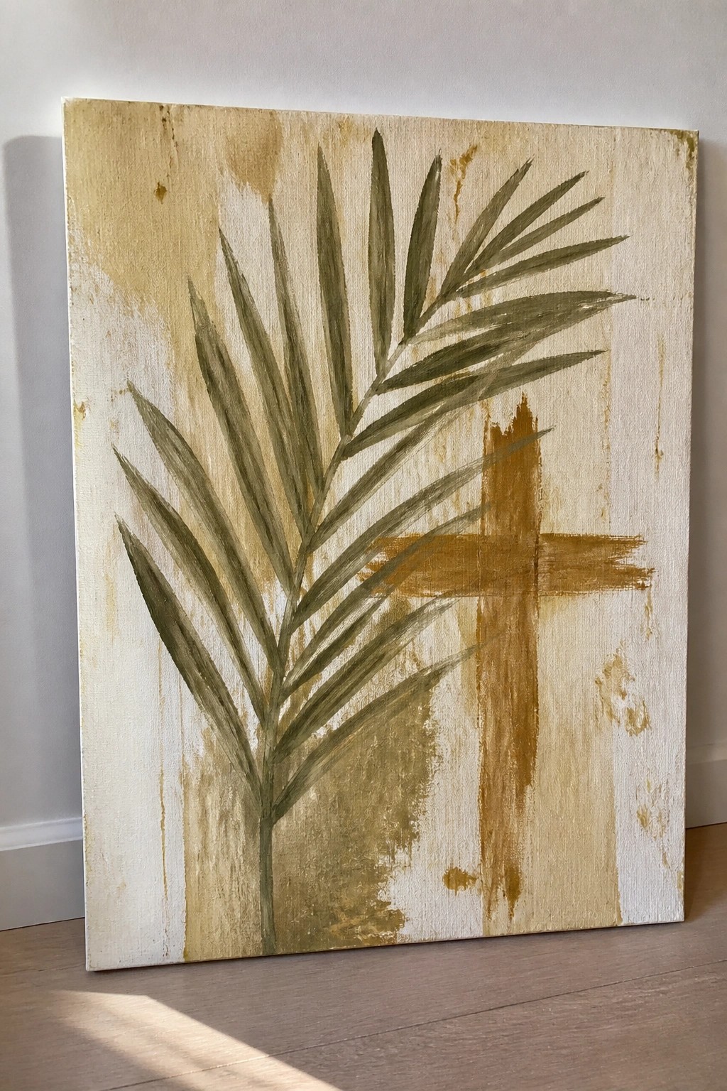 Abstract painting of green palm frond beside brown cross on textured beige canvas.