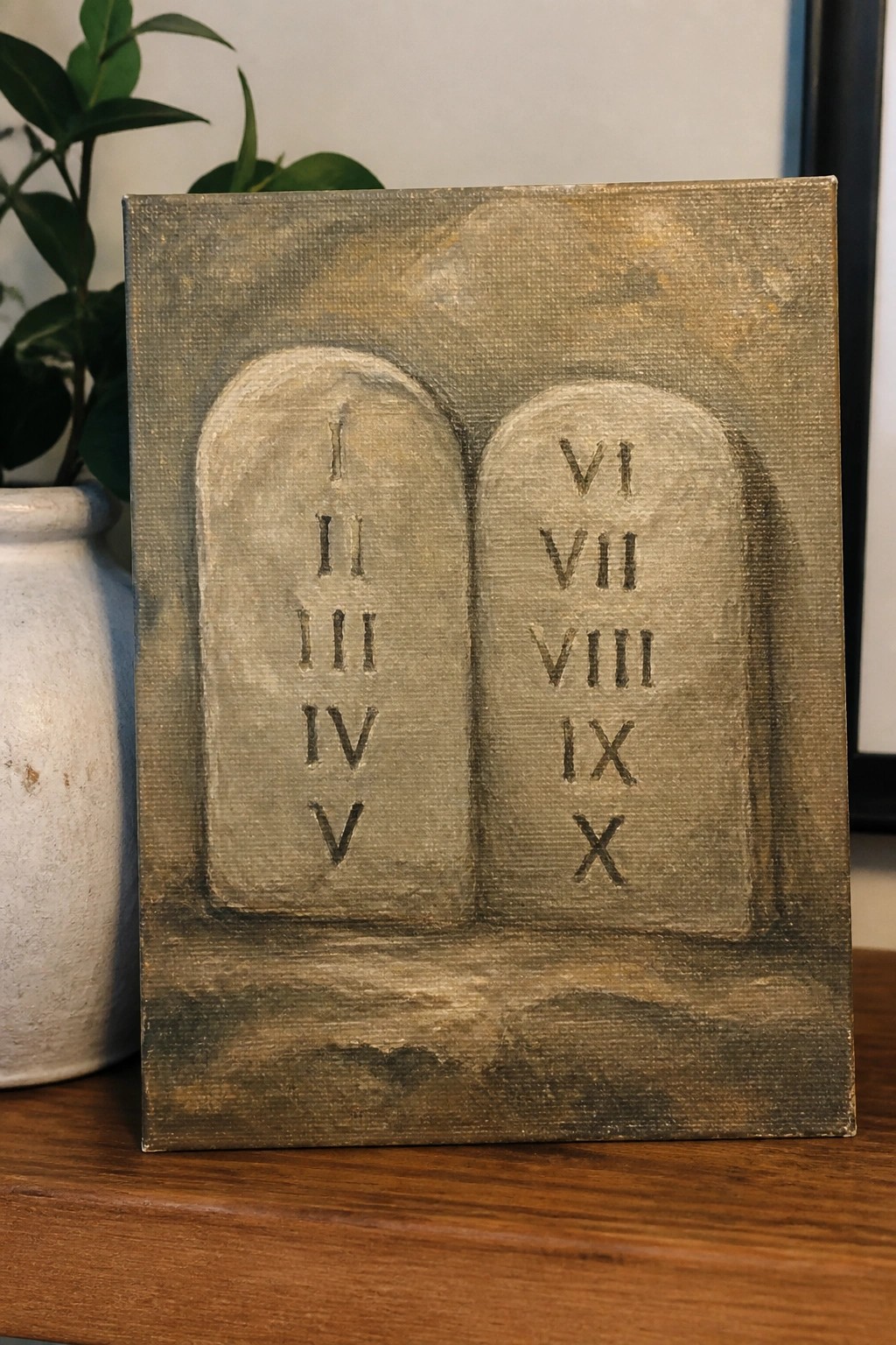 Stone tablets with Roman numerals I-X painted on canvas atop wooden table with plant nearby