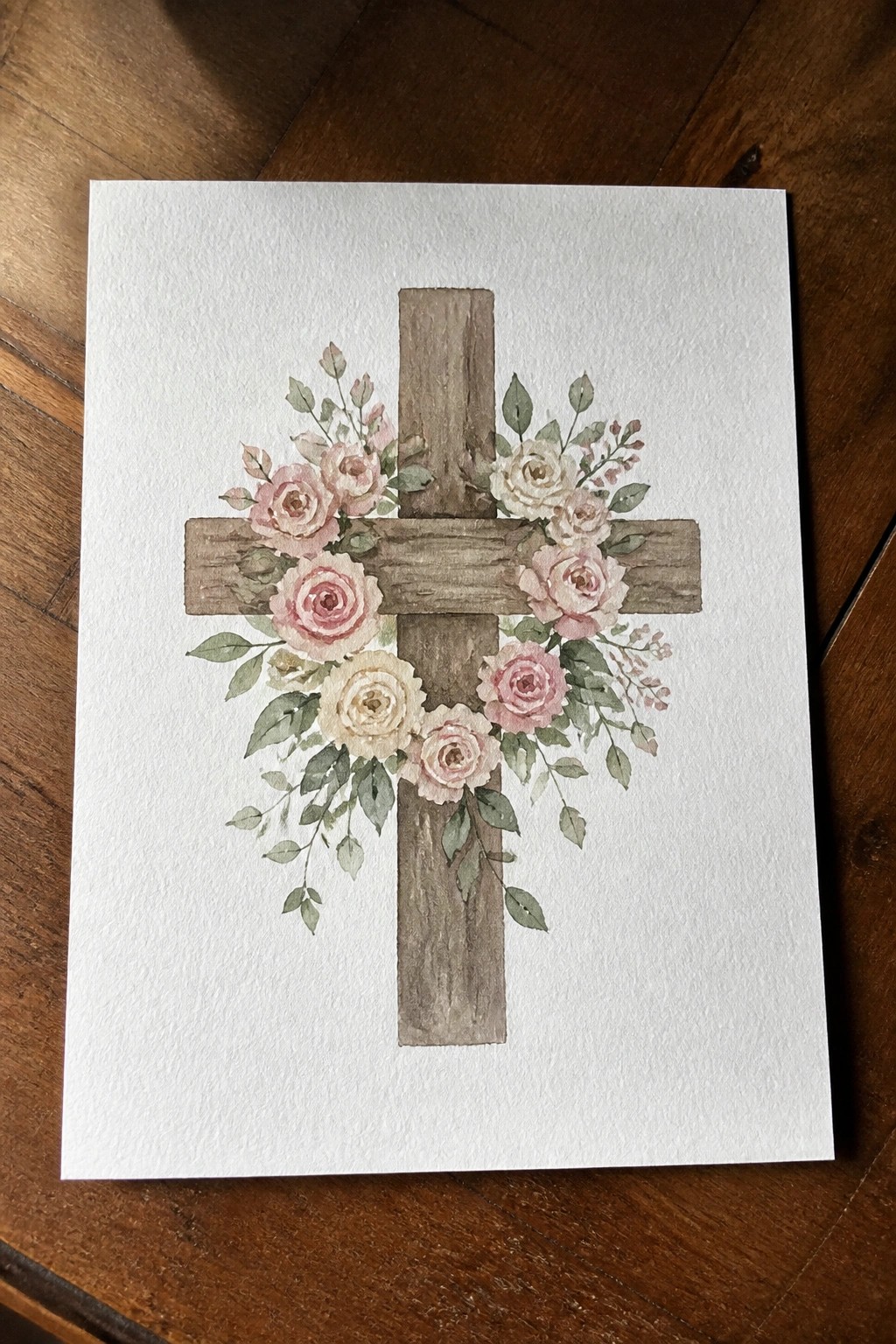 Watercolor painting of rustic wooden cross with pink and white roses and green leaves.