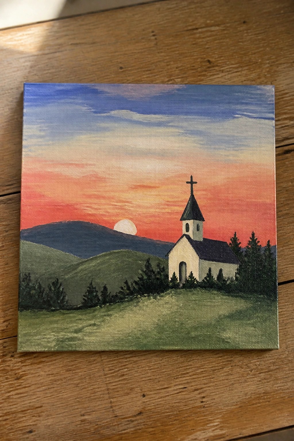 Vibrant sunset painting of white church with cross amid rolling green hills.
