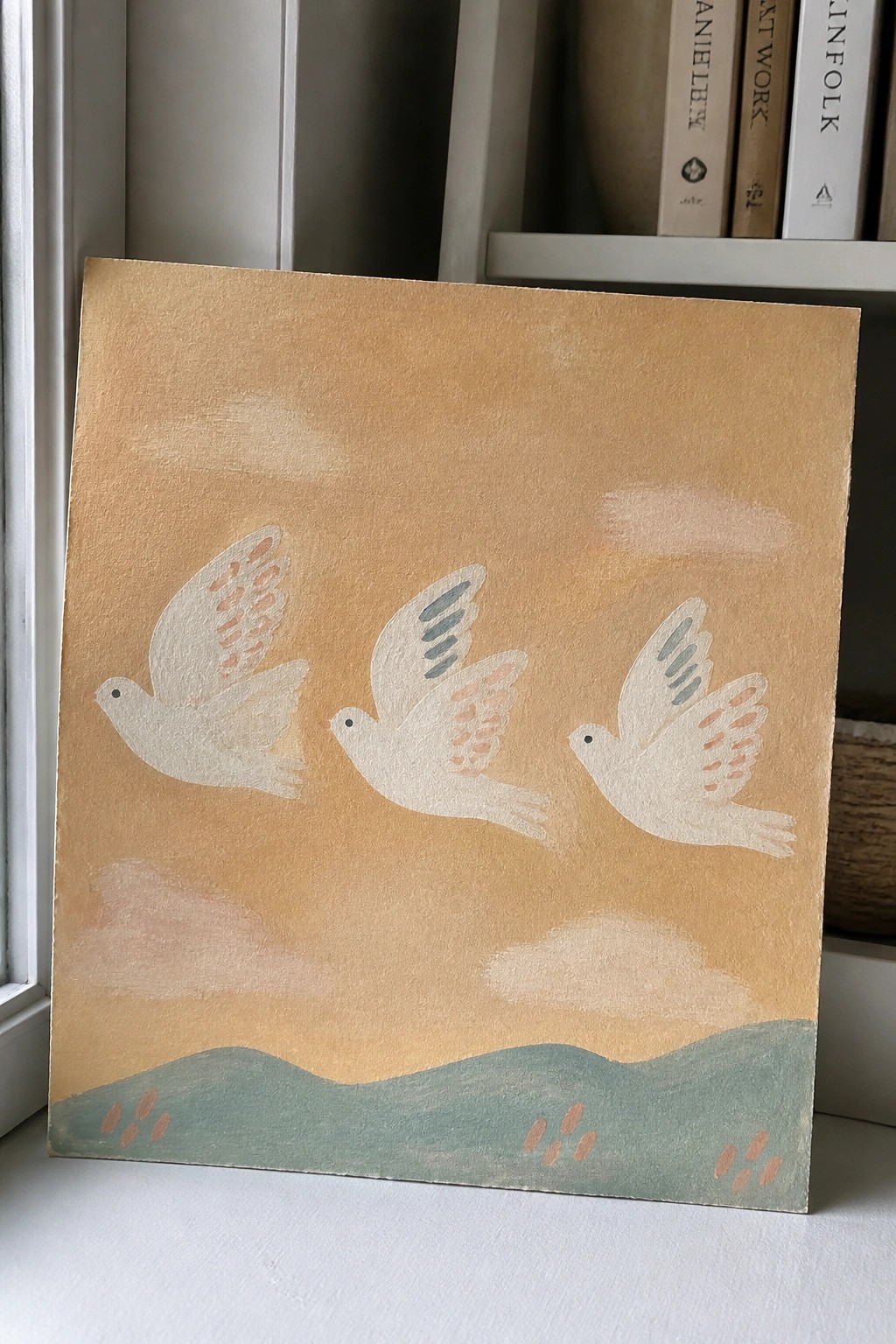 Three white birds flying over green hills in a peach sky painting