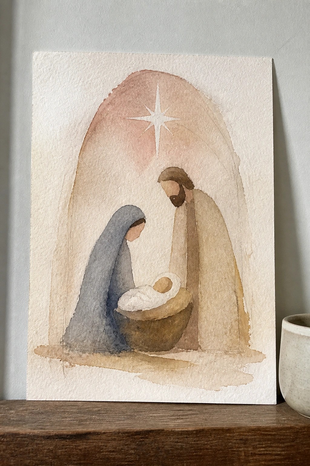 Watercolor nativity with Mary in blue veil, Joseph in tan robe, baby in manger under star