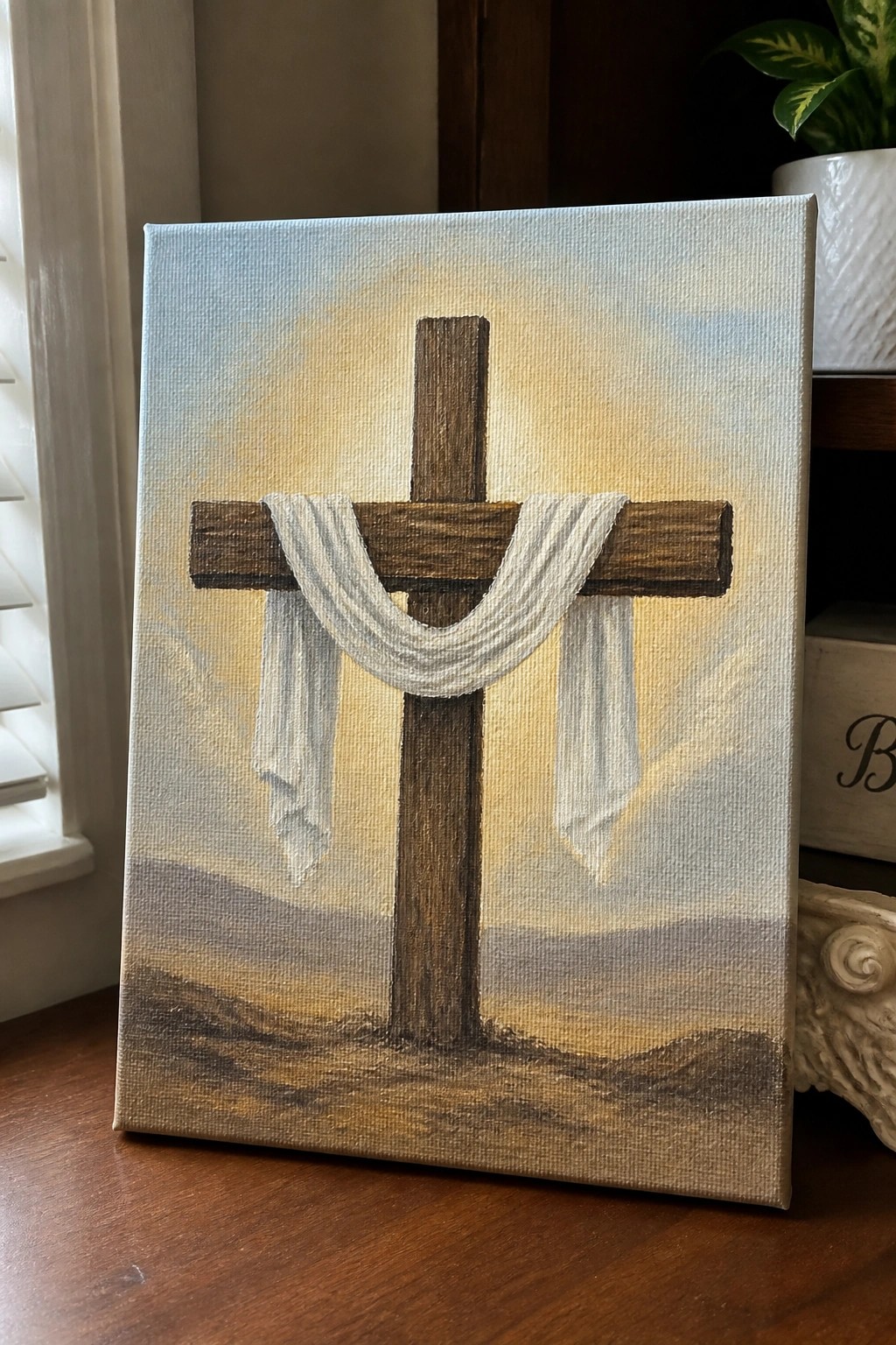 Realistic painting of wooden cross with white cloth draped over hilly landscape at sunset