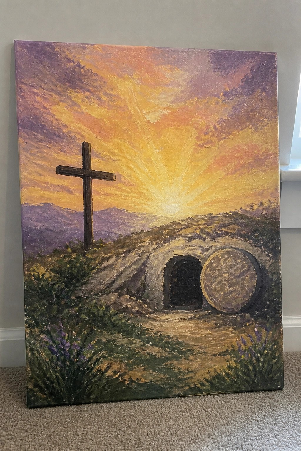 Painting of empty stone tomb with rolled boulder beside wooden cross at vibrant sunrise