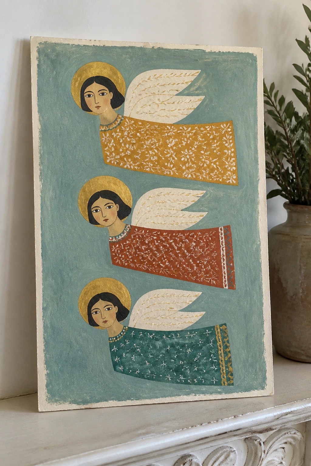 Three angels with golden halos and wings in patterned yellow, red, and green robes on teal.
