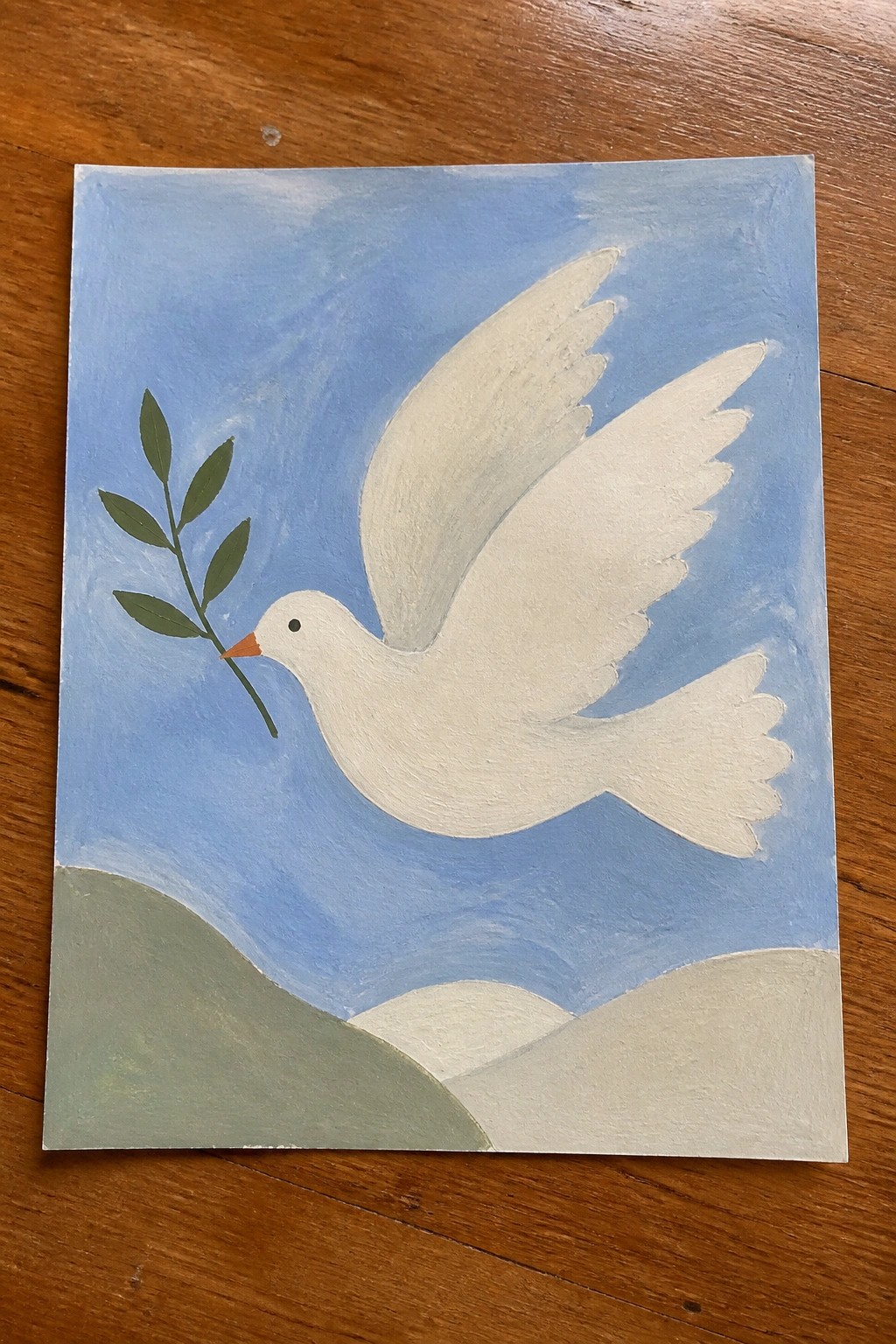 White dove flies in blue sky holding green olive branch above rolling hills