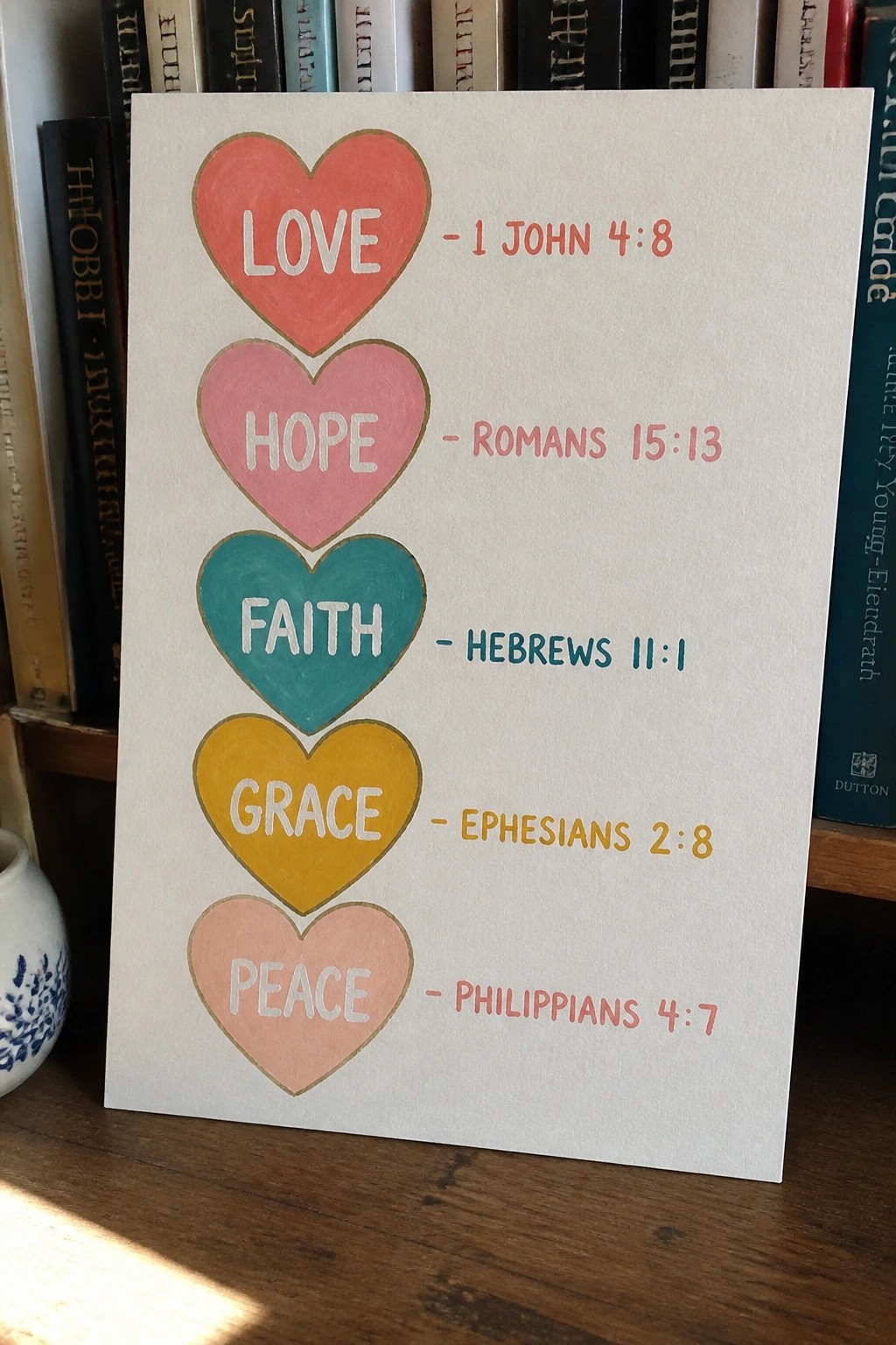 Stacked colorful hearts with love hope faith grace peace and Bible verses on card before books