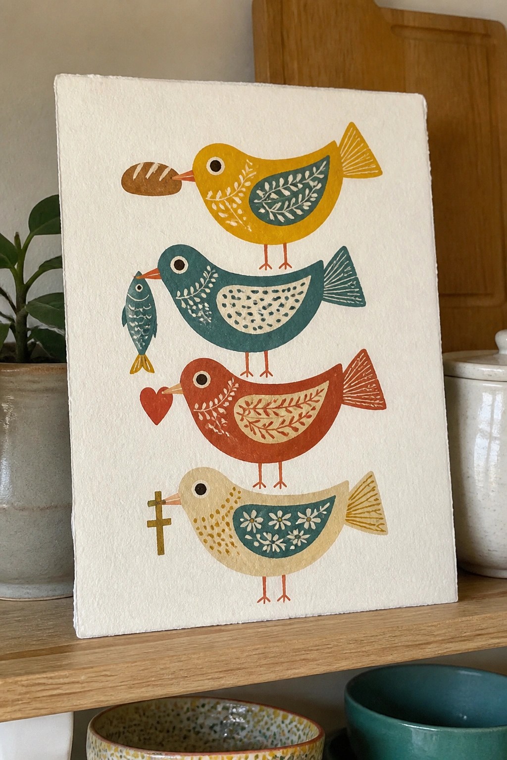 Four stacked colorful folk-art birds holding bread, fish, heart, and cross.