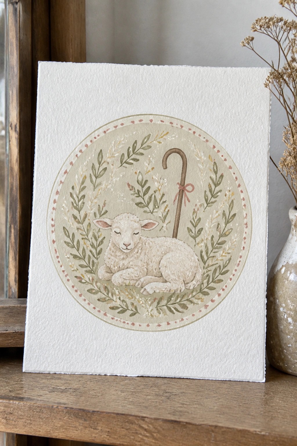 Watercolor of sleeping lamb with shepherd's crook in leafy floral wreath on paper