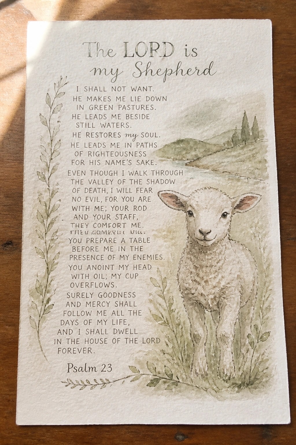 Watercolor Psalm 23 text beside a white lamb in green hills and foliage.