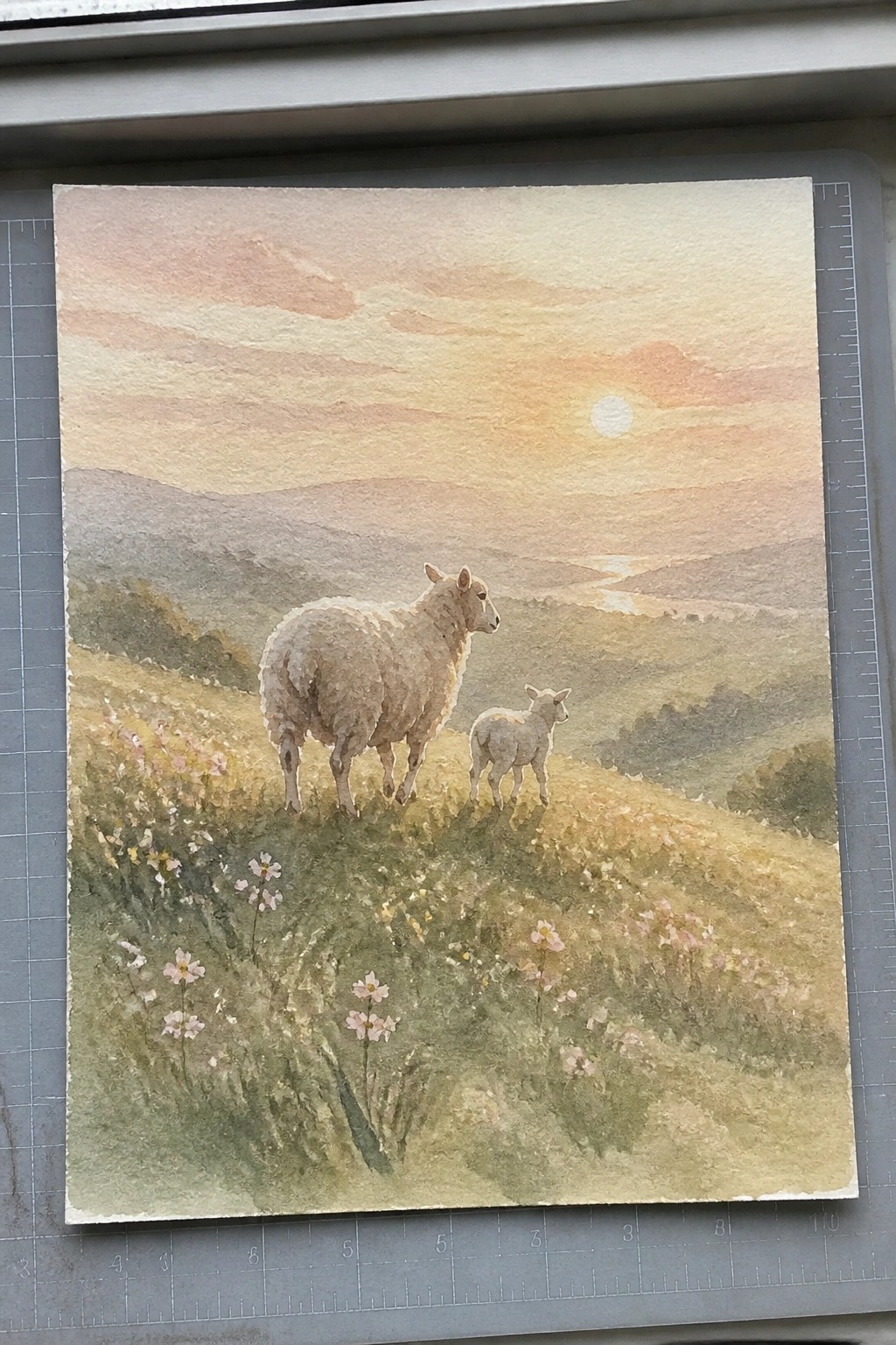Watercolor of ewe and lamb amid wildflowers on a hill under a pink sunset sky