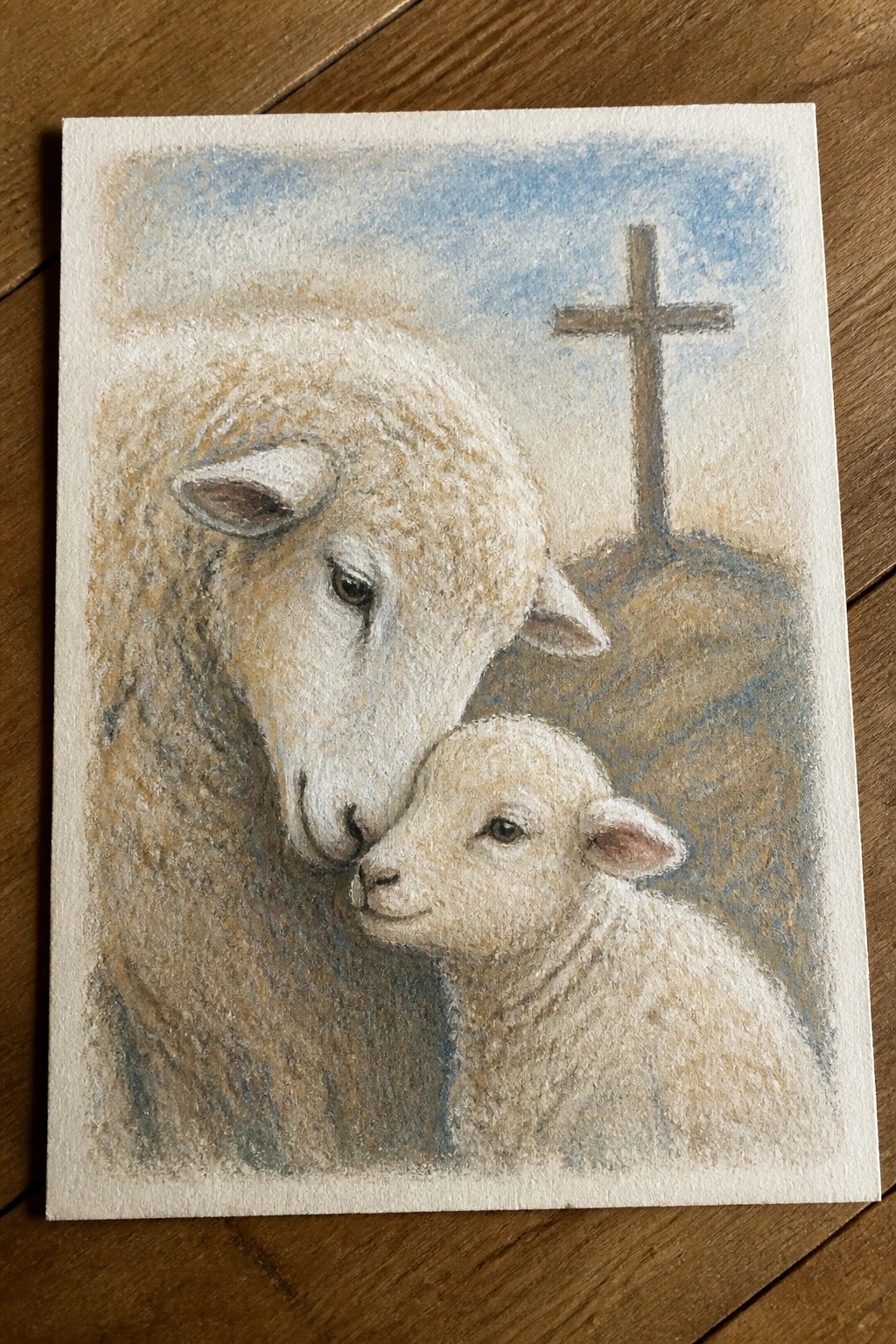 Adult sheep and lamb nuzzling near wooden cross on grassy hill under blue sky