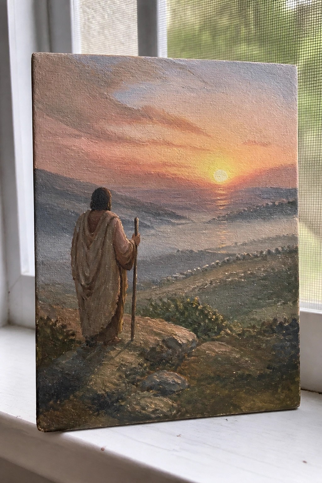Robe-clad figure with staff overlooks orange sunset across misty hills with distant sheep.