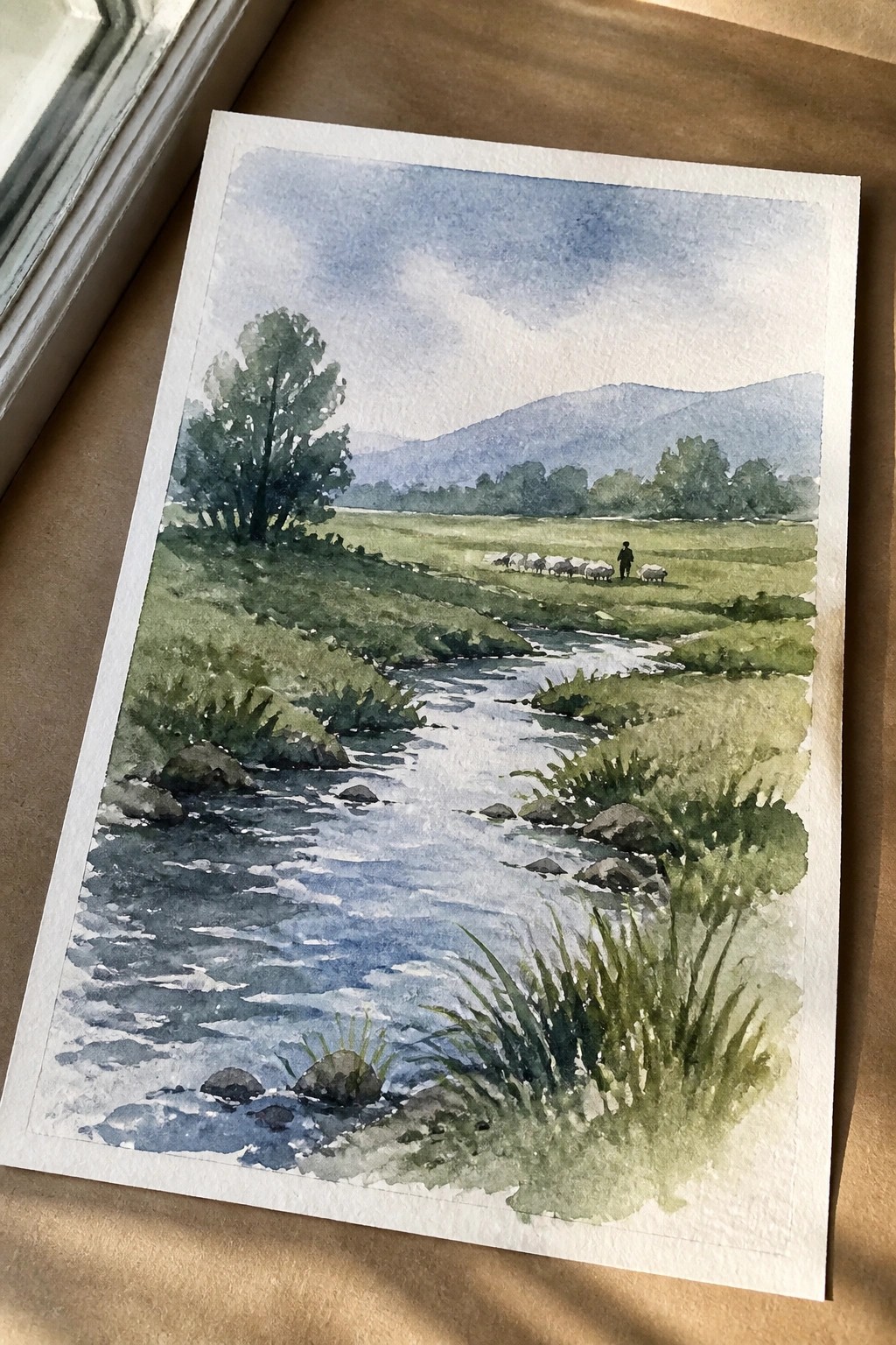 Watercolor landscape of stream through green fields with shepherd, sheep, trees and distant mountains.