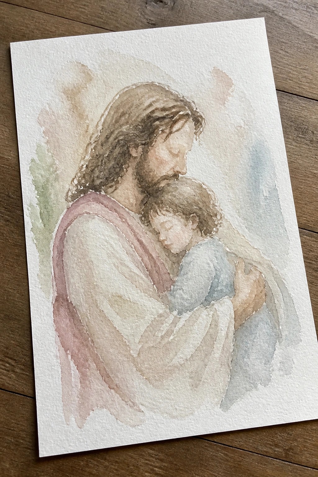 Watercolor of Jesus in white robe holding sleeping child in soft pastels.