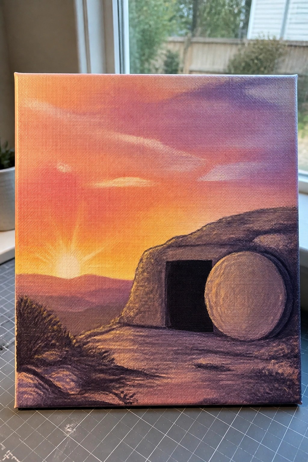Vibrant sunset painting of rocky cave with dark entrance and large circular stone.