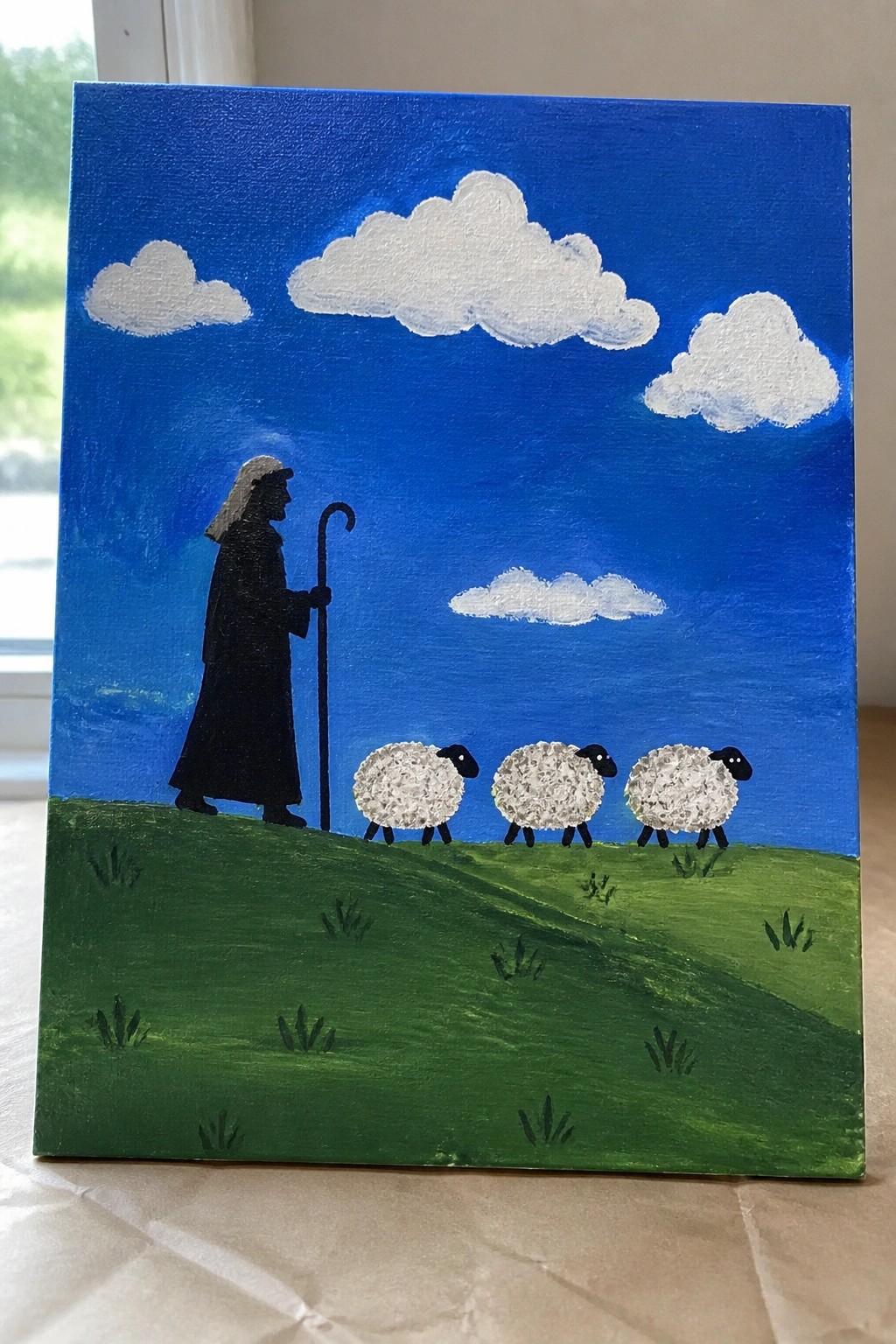 Black-robed shepherd with staff leads three sheep on green hill under blue sky