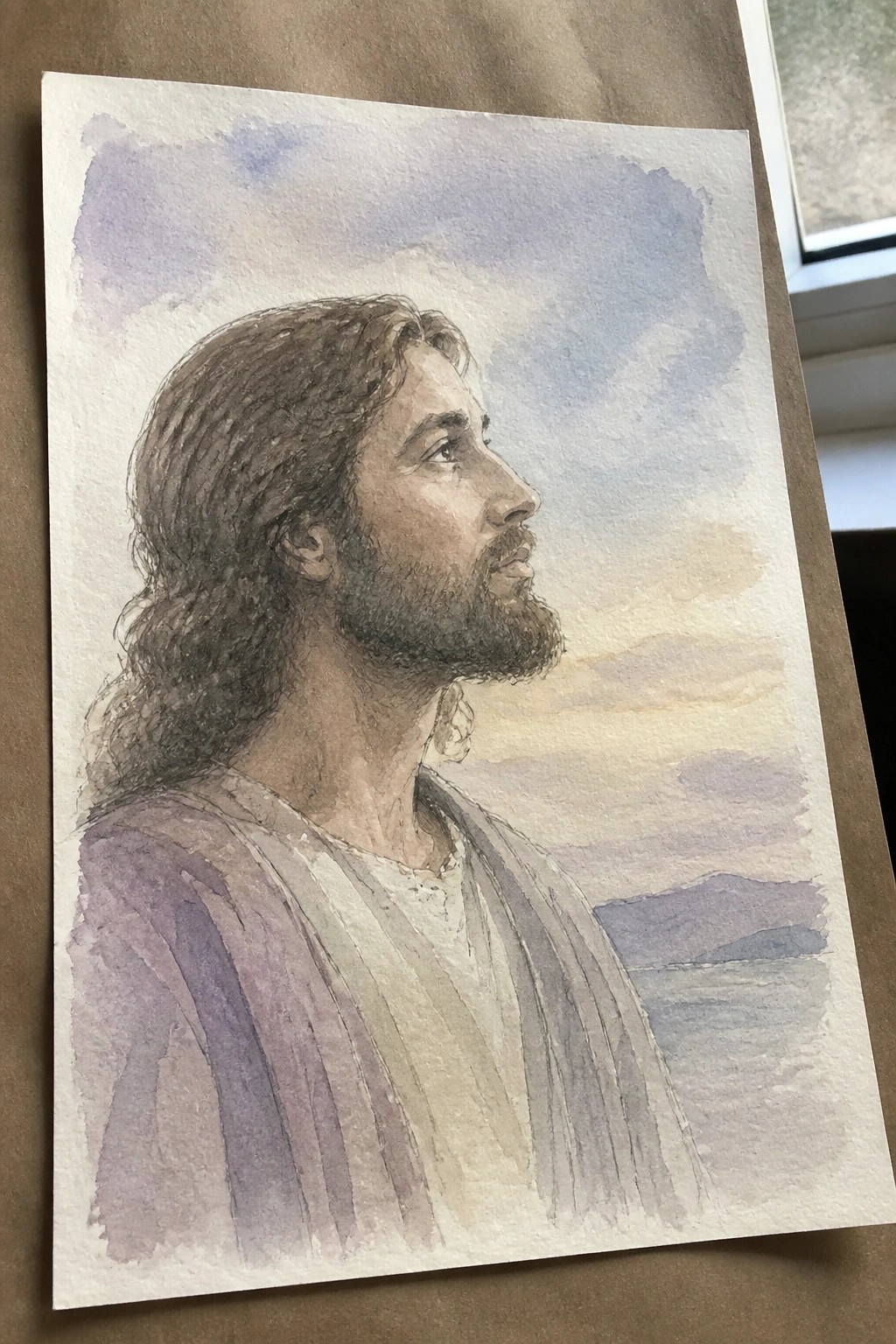 Watercolor portrait of bearded man with long hair in profile against sunset landscape