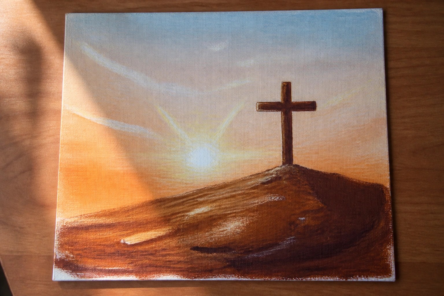 Canvas painting of a cross on a hill under a vibrant sunset sky.